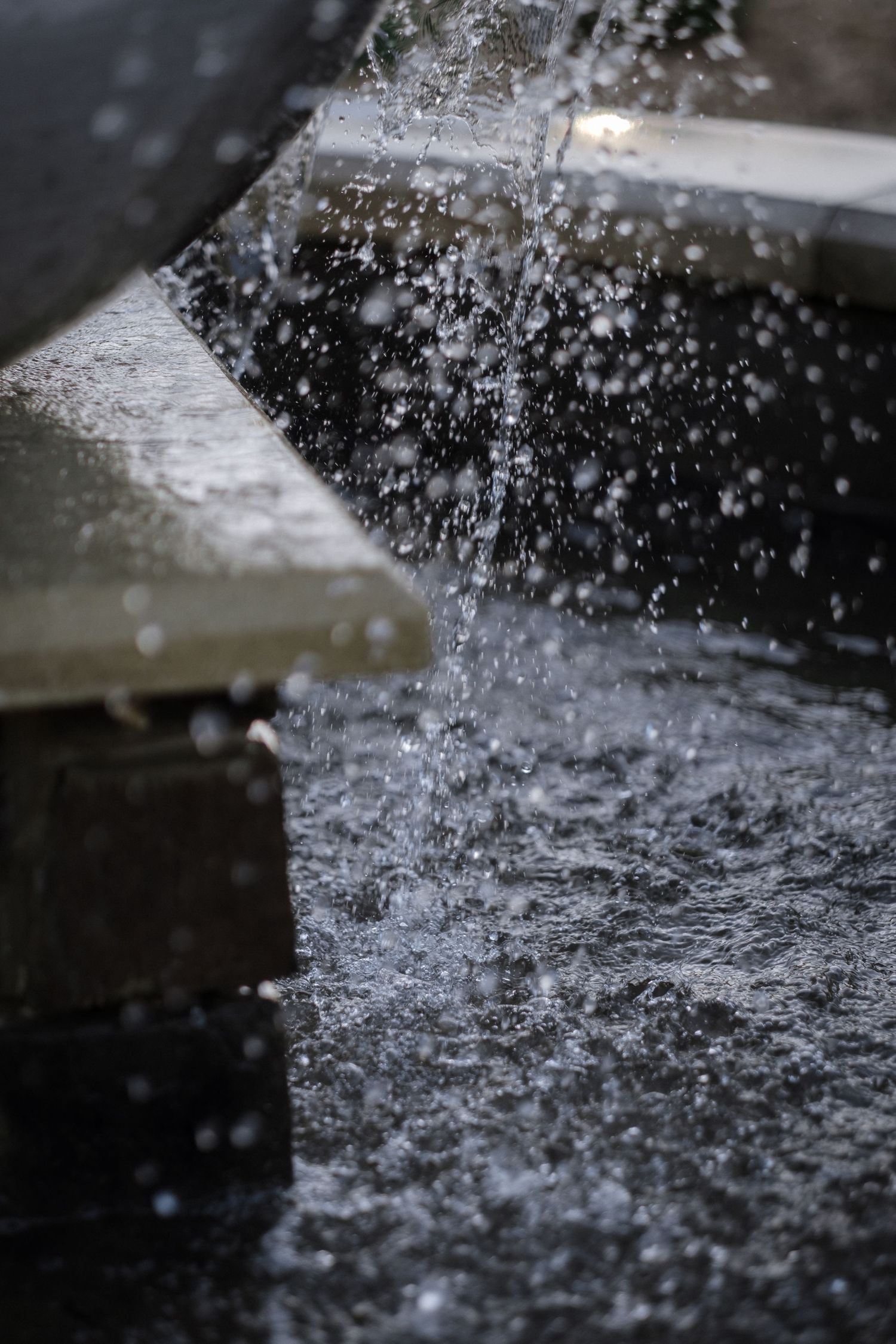 Water splashing and cascading from a stone fountain feature, with droplets frozen in motion against a dark background.