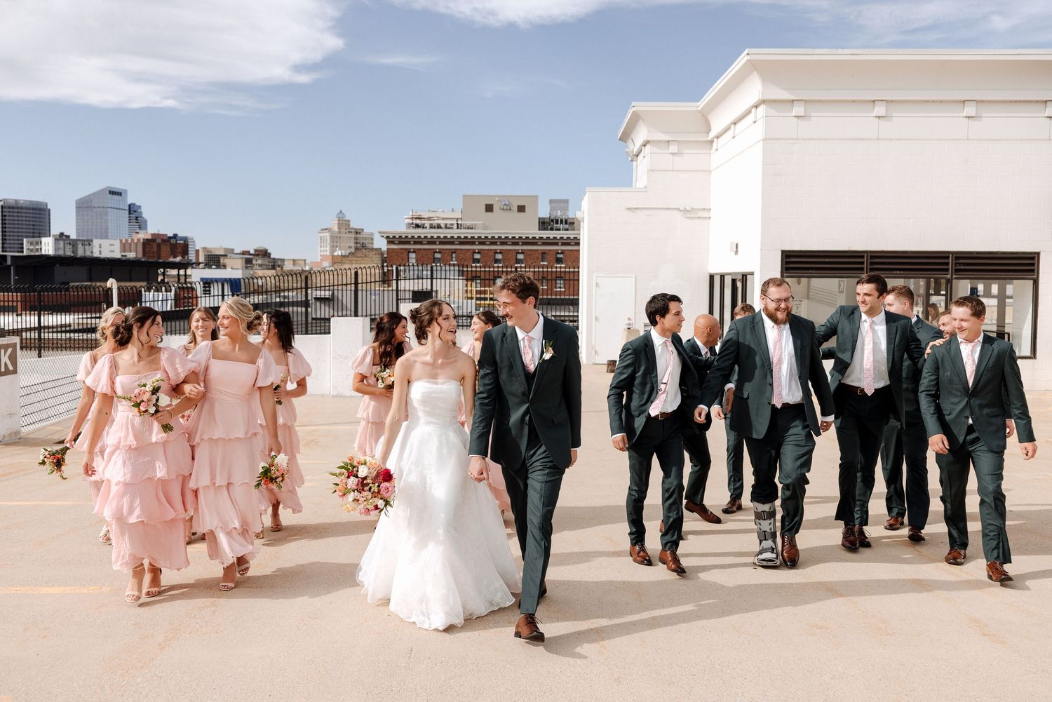 Wedding party walks on rooftop with bridesmaids in pink and groomsmen in dark suits.