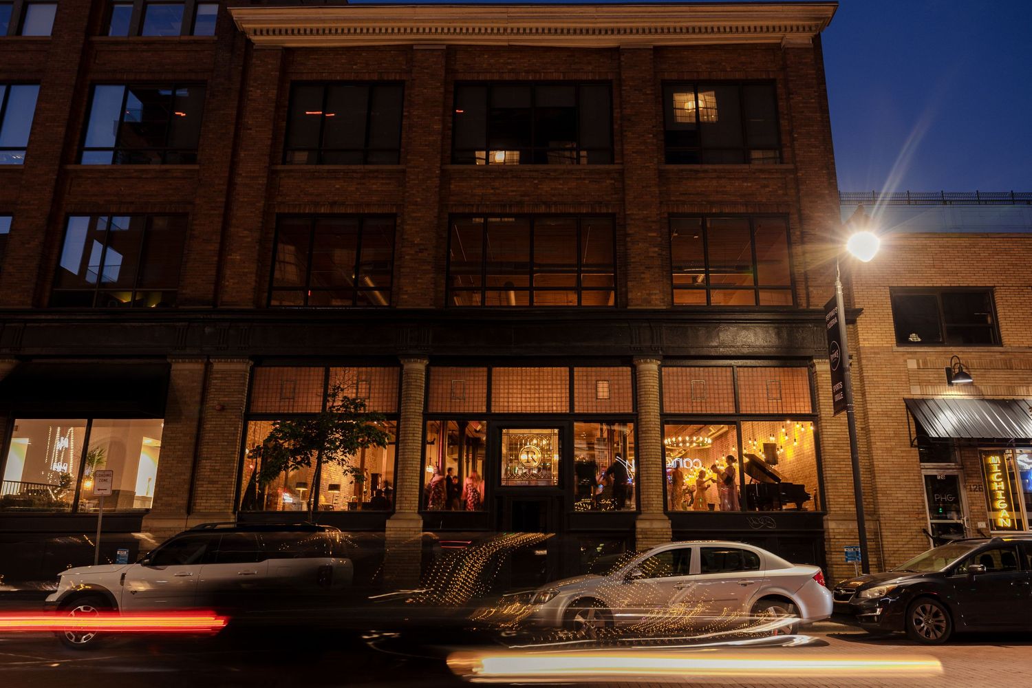 Elegant urban wedding venue glows warmly from inside a multi-story brick building at night.
