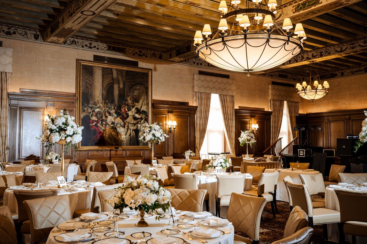 Grand wedding reception hall with tall floral centerpieces, chandeliers, and ornate painted ceiling.