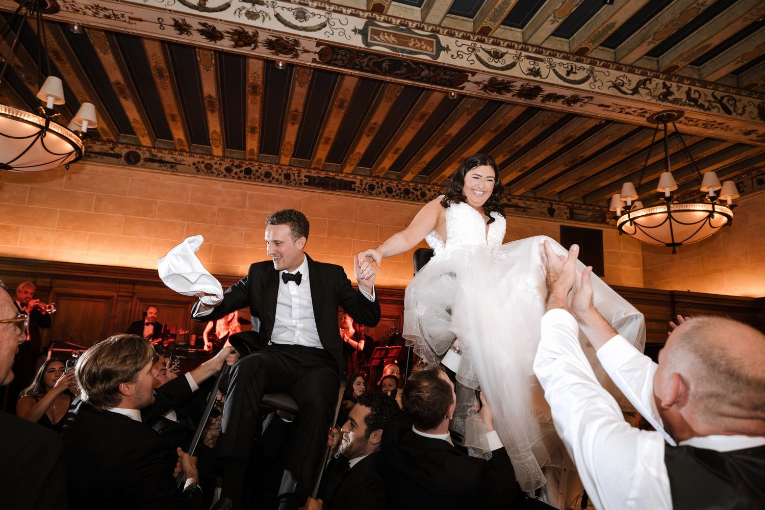 Newlyweds raised on chairs by cheering guests during lively hora wedding dance.