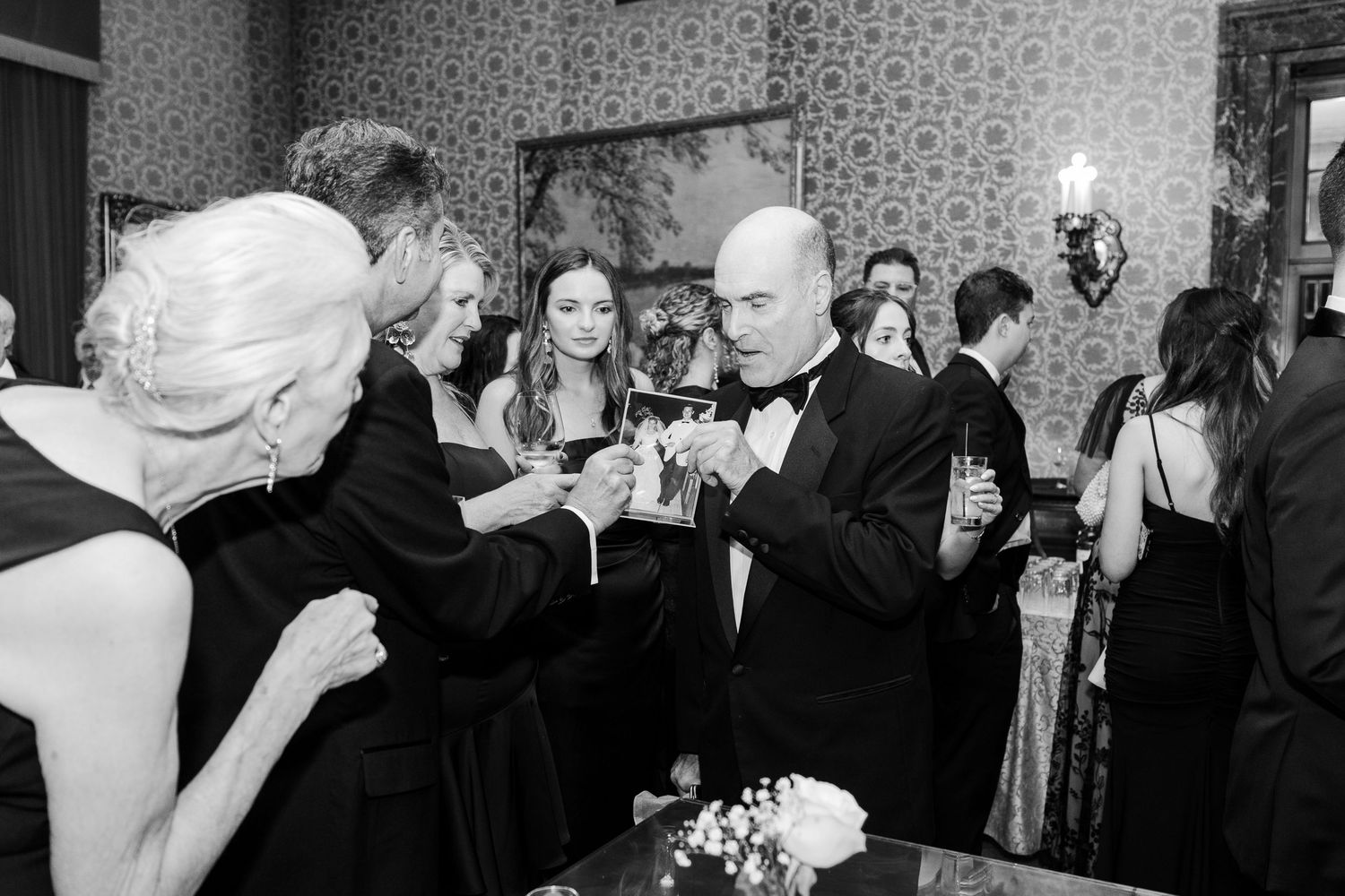 Elegant black and white photo of guests in formal attire toasting drinks at a sophisticated evening reception.