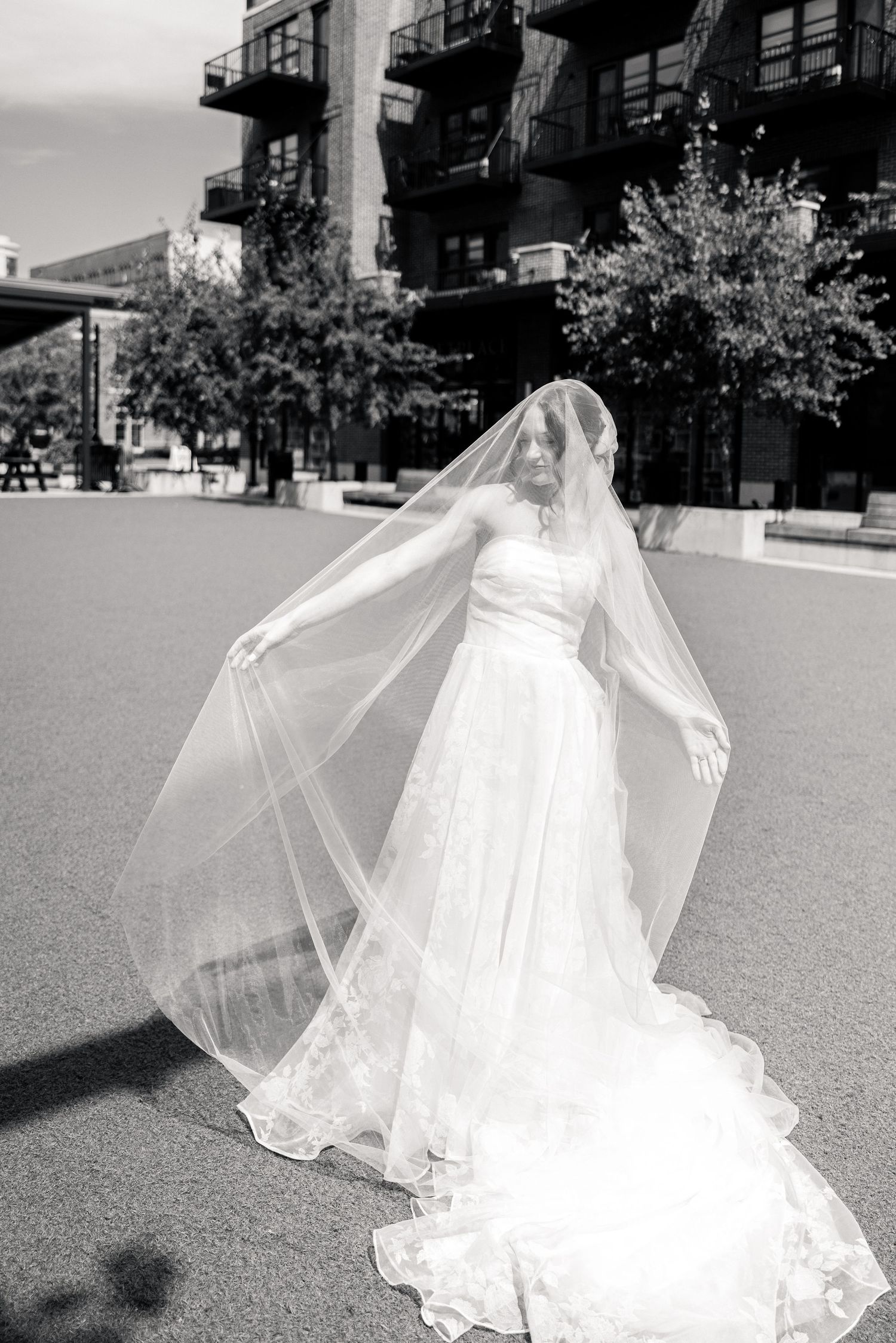 Black and white photo of a bride spreading her cathedral veil wide open in an urban outdoor setting.