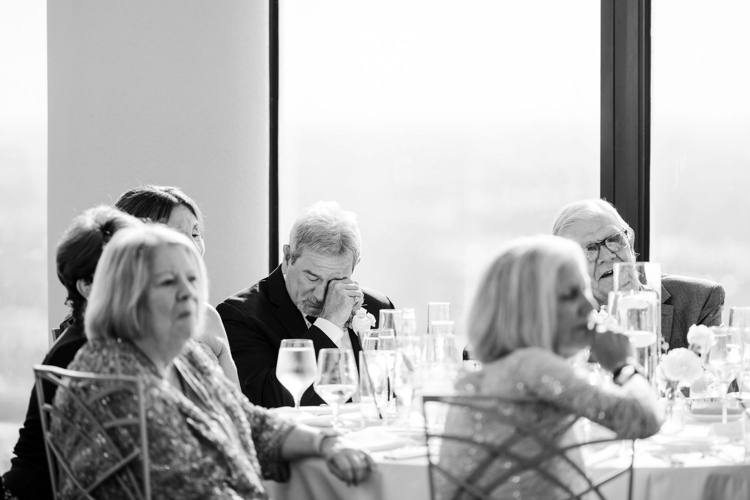 Black and white photo of elegantly dressed guests seated at tables during a formal dinner event or wedding reception.