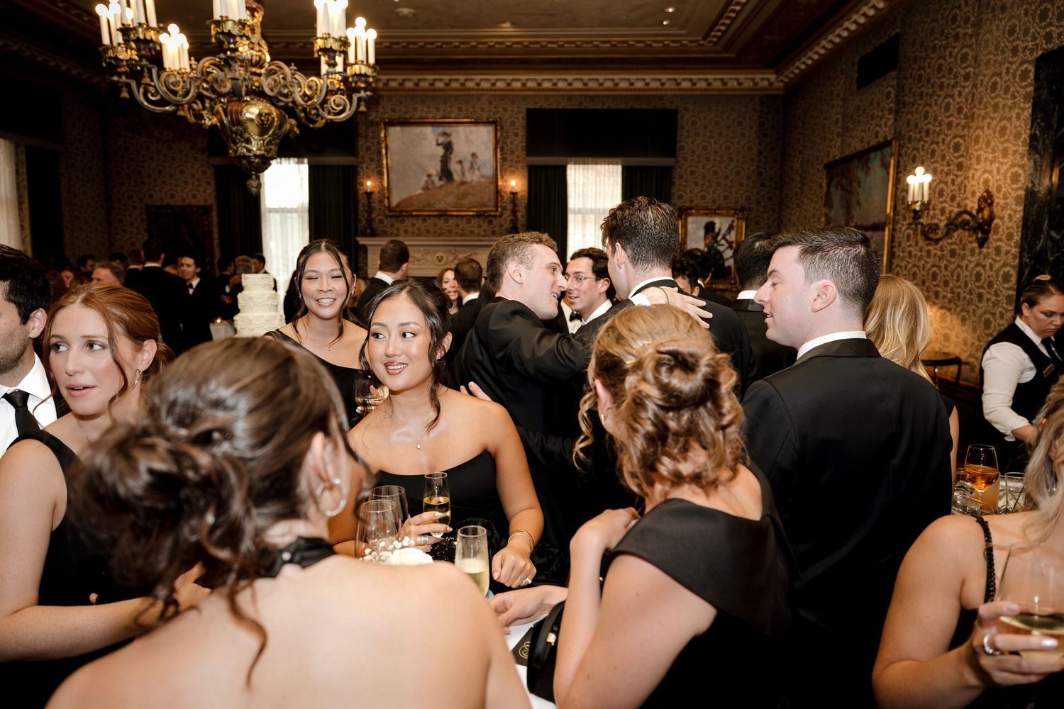 Elegantly dressed wedding guests mingle and celebrate during a black tie reception in a grand ballroom.