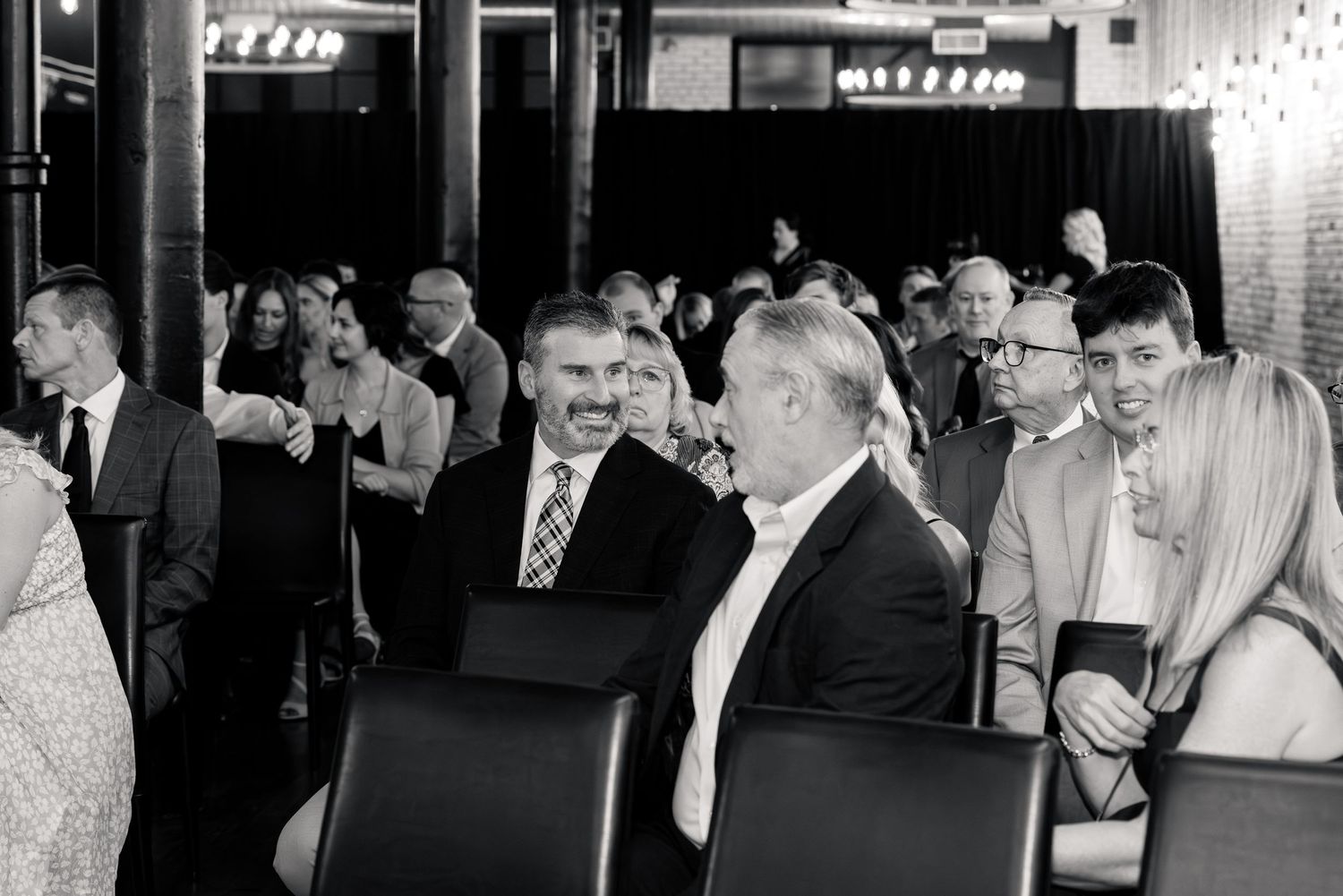 Black and white photo of wedding reception guests mingling and conversing in an elegant event space.