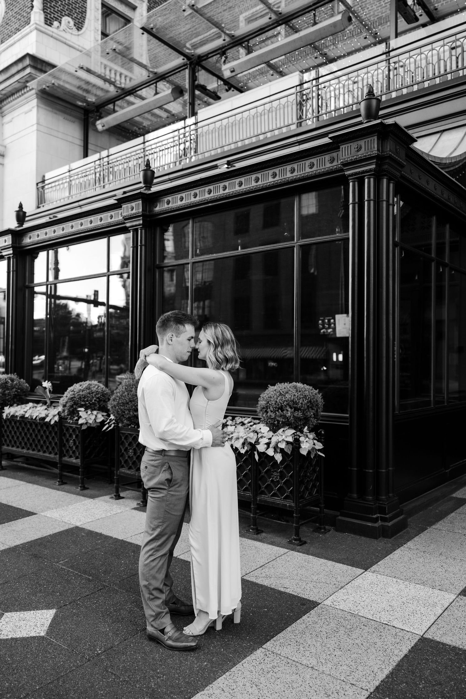 Black and white photo of couple embracing romantically outside an ornate building with flowers.