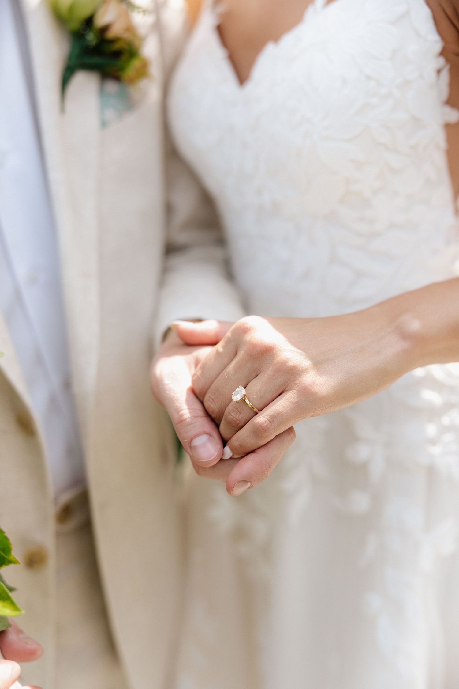 Close-up of bride and groom holding hands showing elegant solitaire diamond engagement ring.