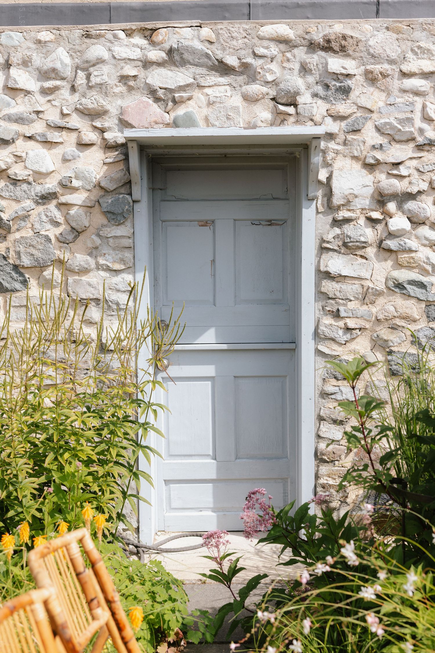 A pale blue wooden door set in a rustic stone wall, surrounded by lush green plants and wildflowers.