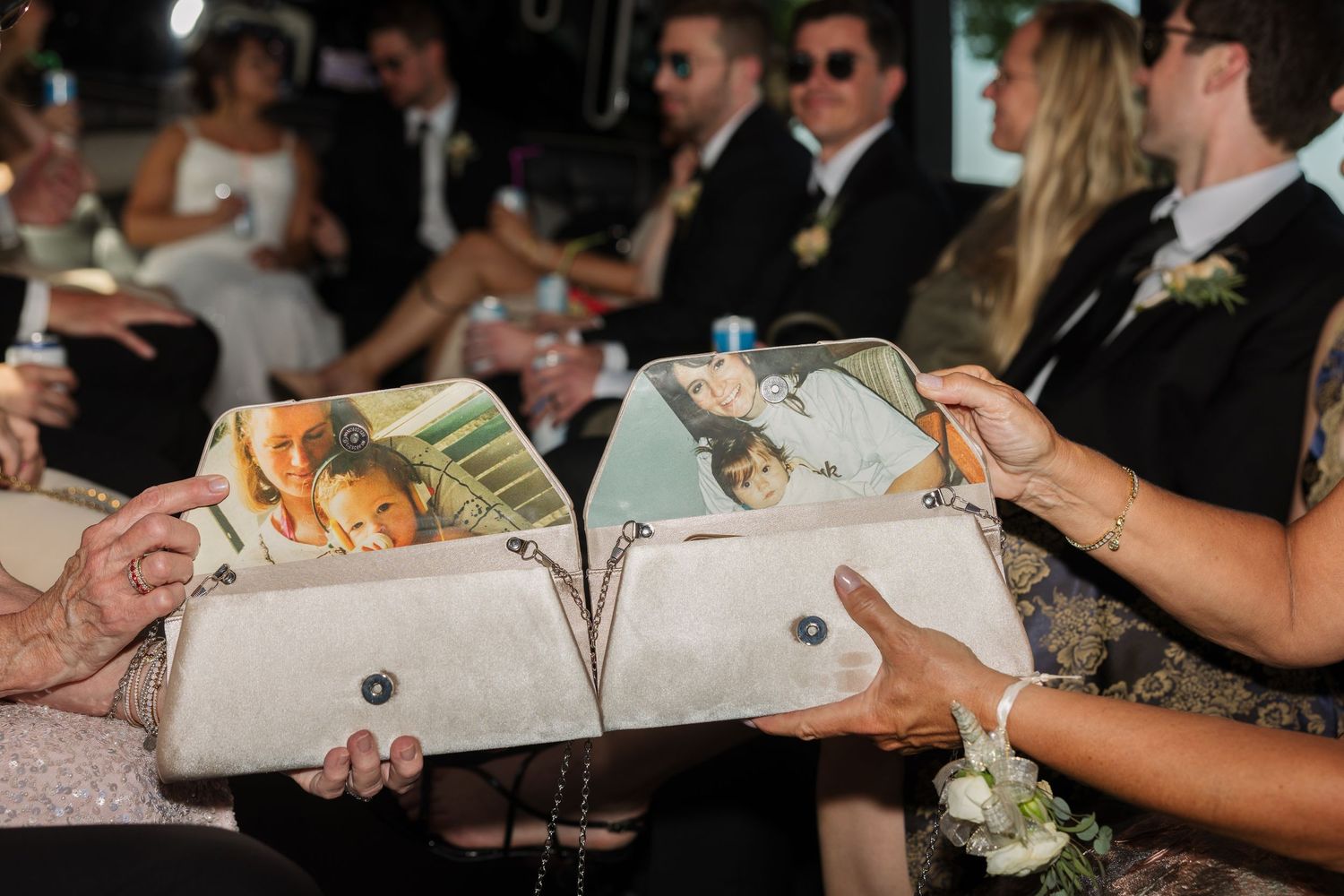 Two white clutch purses with photo prints held by wedding guests, bridal party seated in background.