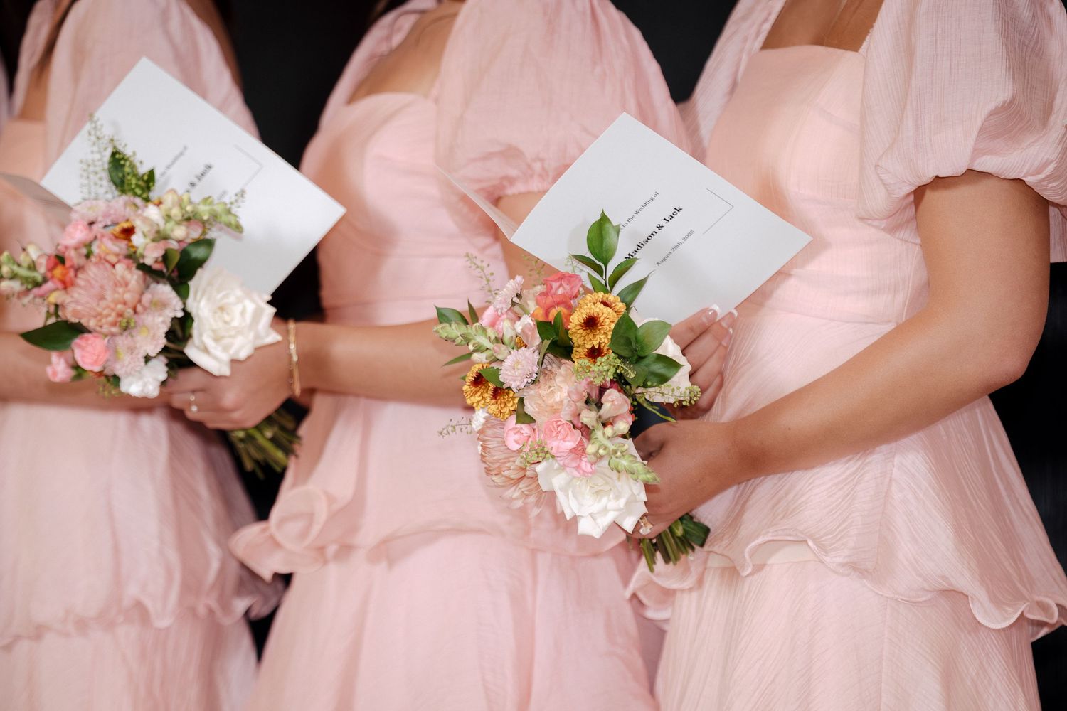 Three bridesmaids in blush pink dresses holding bouquets of pink and white flowers at a wedding ceremony.
