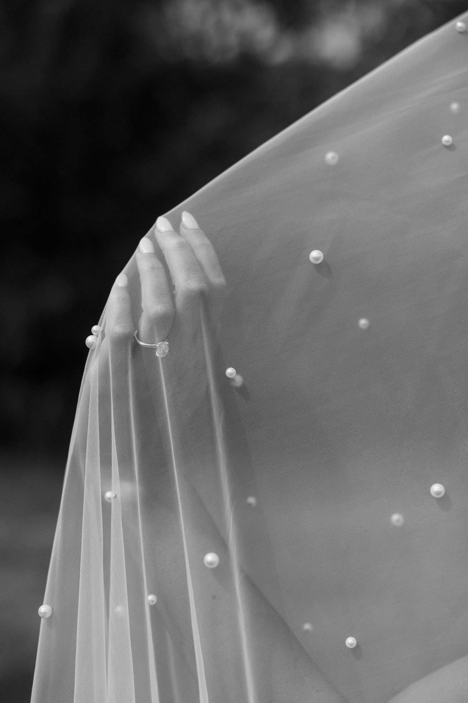 Black and white close-up of a bridal veil with pearl embellishments draped over a shoulder.