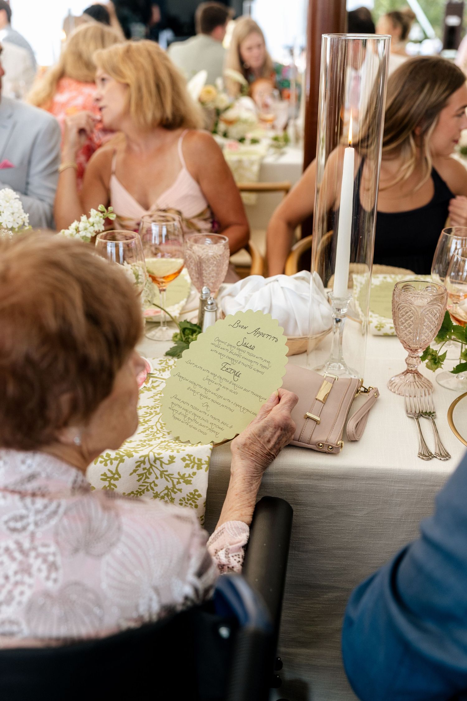 Elderly woman reading a green menu card at an elegant wedding reception dinner table with floral decor.