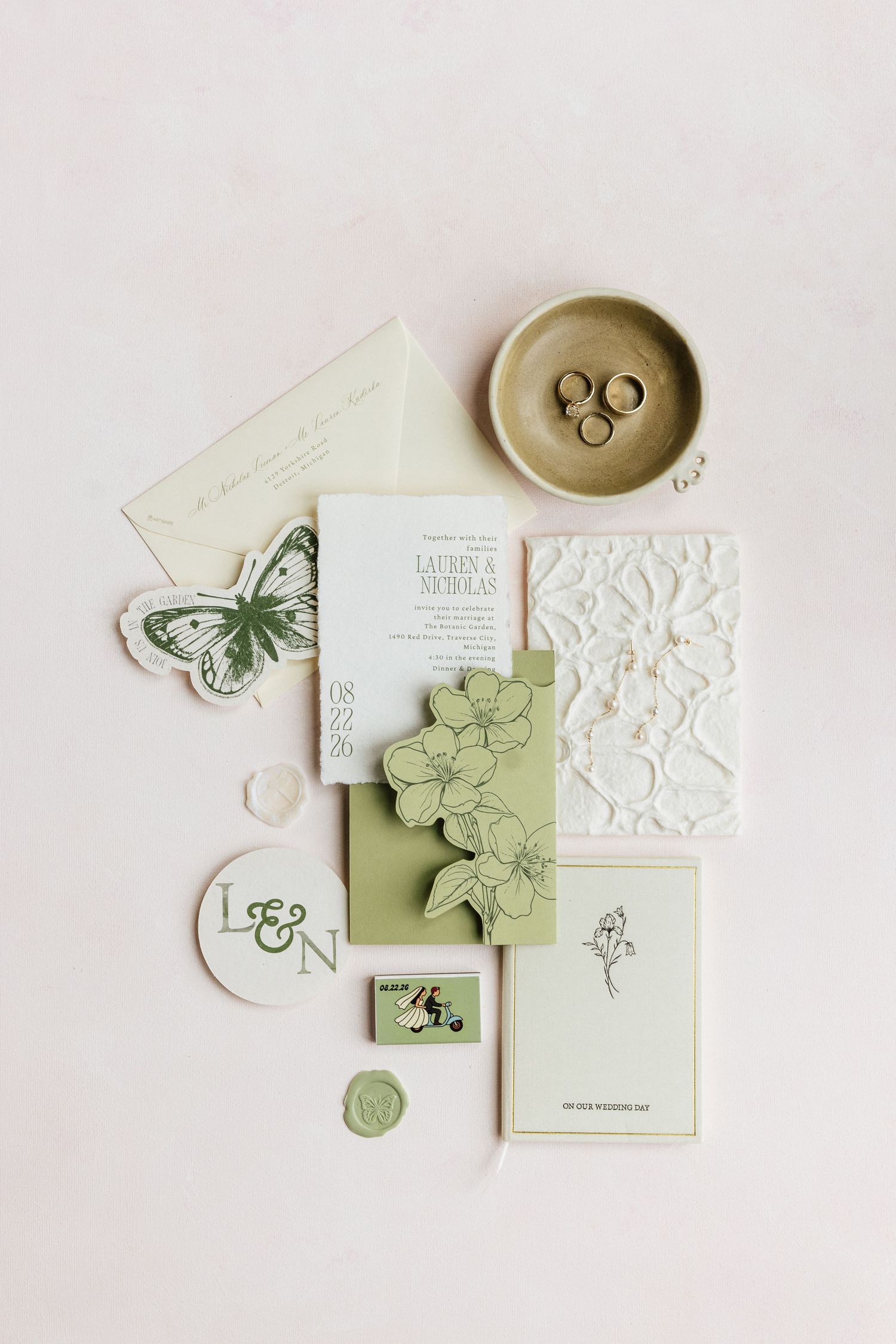 Elegant sage green wedding stationery suite with butterfly motifs, floral embossing, wax seal, and gold rings on a neutral background.