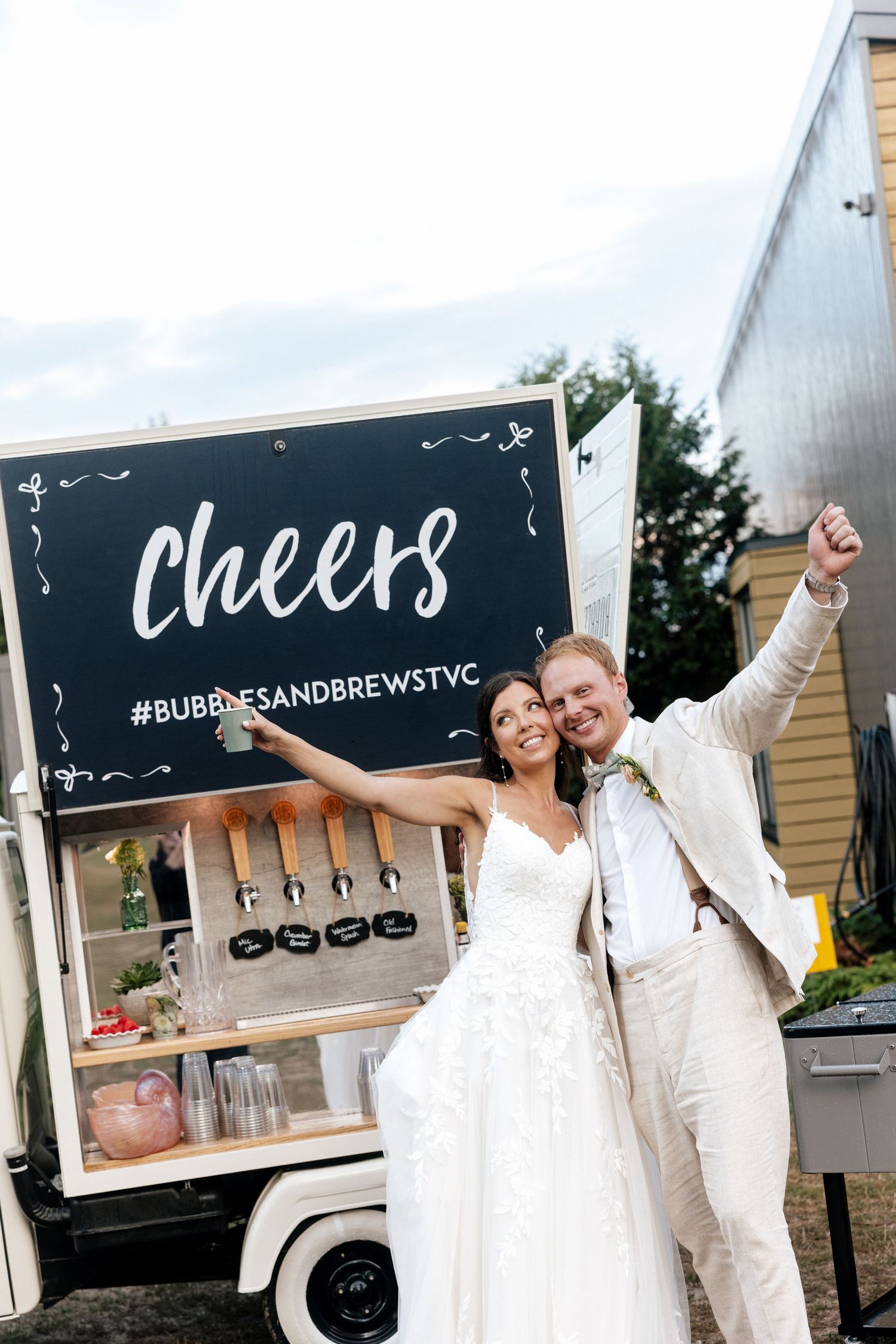 Bride and groom celebrate in front of a Cheers bar truck at their wedding reception.