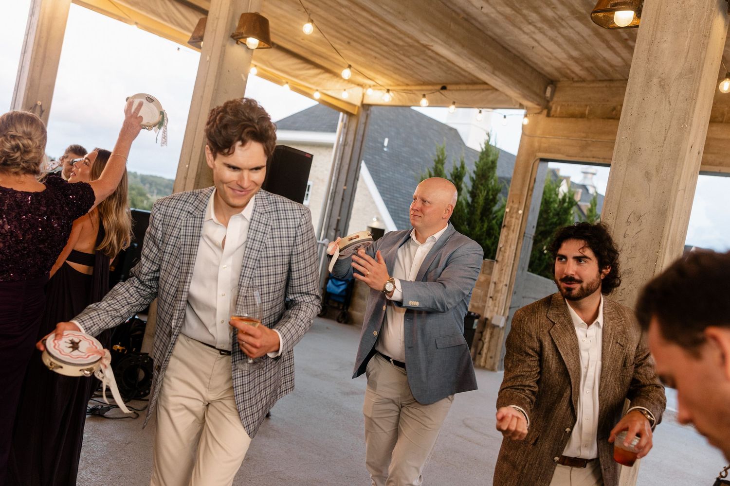 Men dancing and celebrating at an outdoor wedding reception venue with string lights.