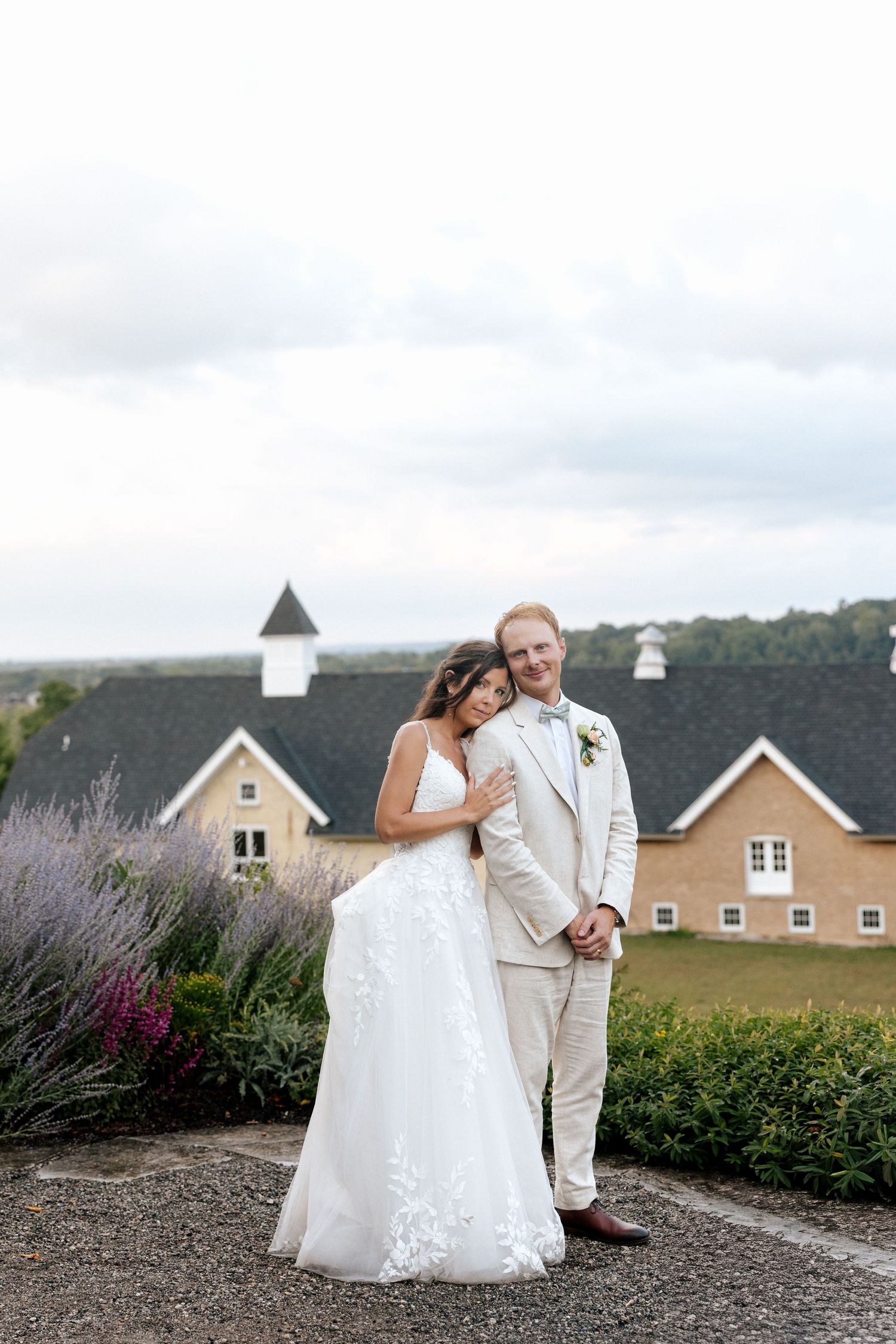 Bride and groom embrace outdoors with a rustic barn venue and lavender gardens in the background on their wedding day.