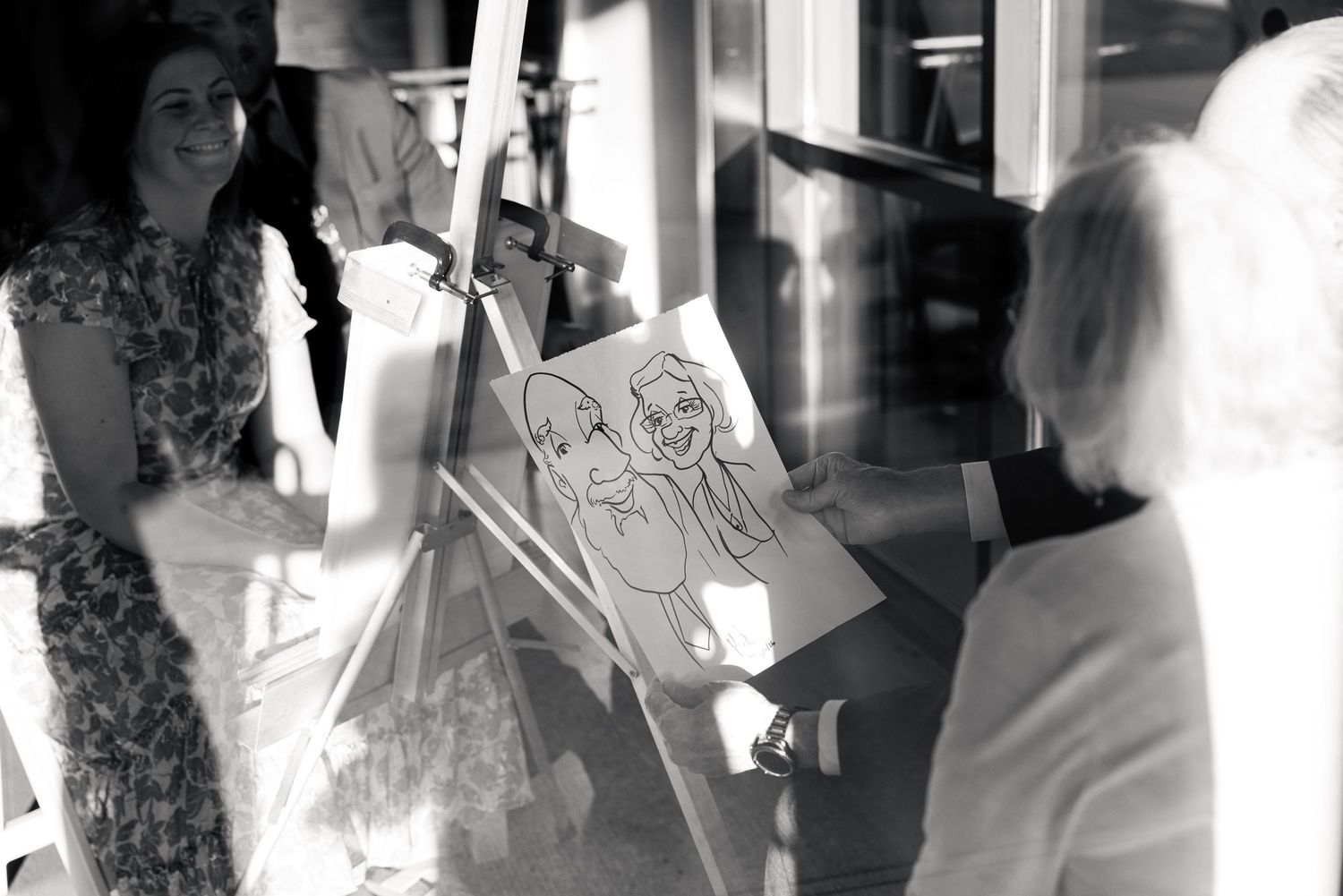 Black and white photo of a caricature artist drawing a portrait on an easel at a social event.