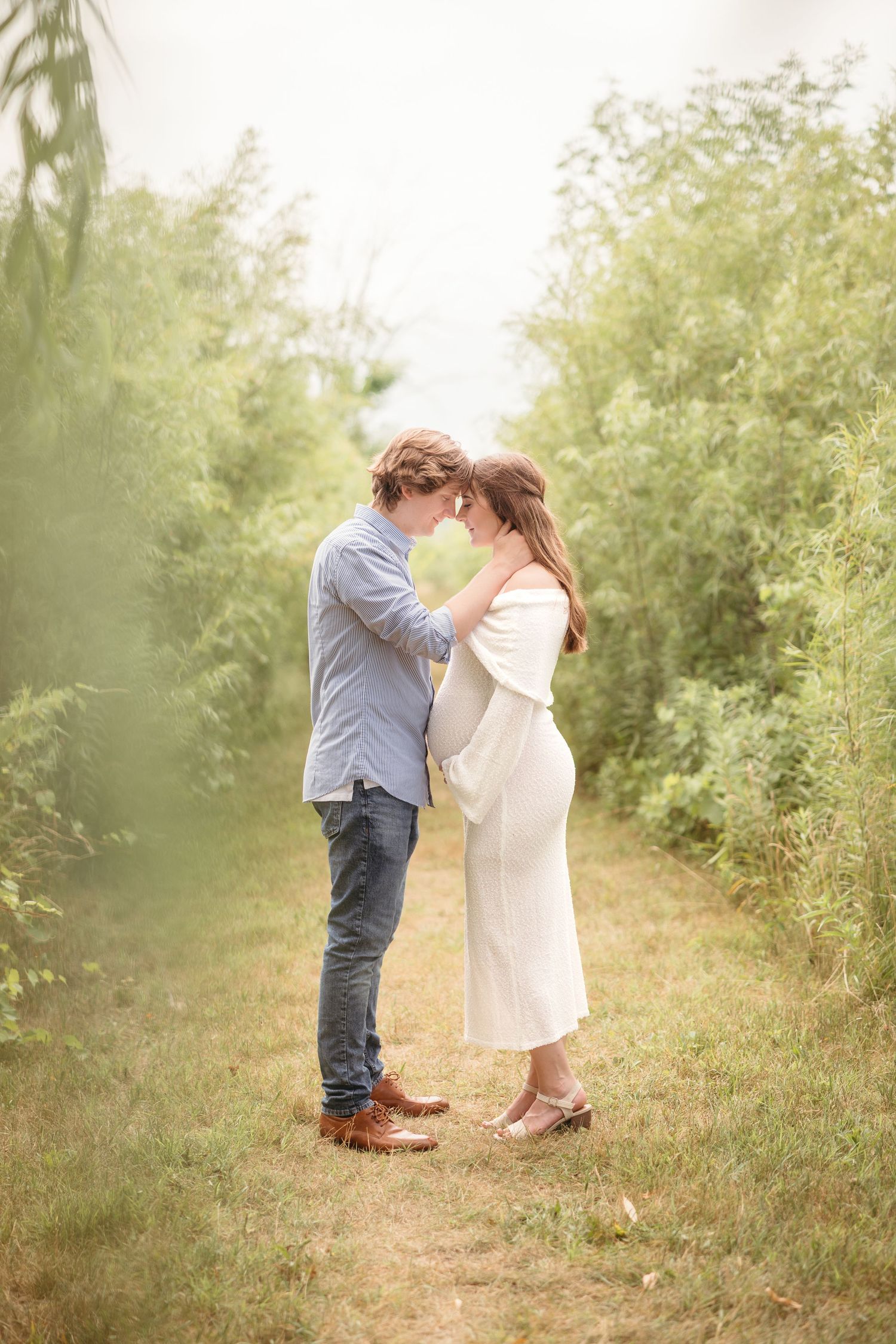 Expecting couple sharing tender forehead touch in lush green garden path.