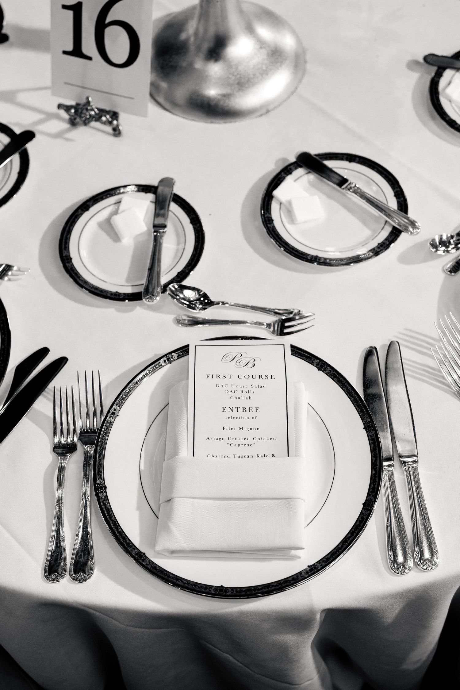 Black and white photo of a formal wedding place setting with menu card, silverware, and charger plate.