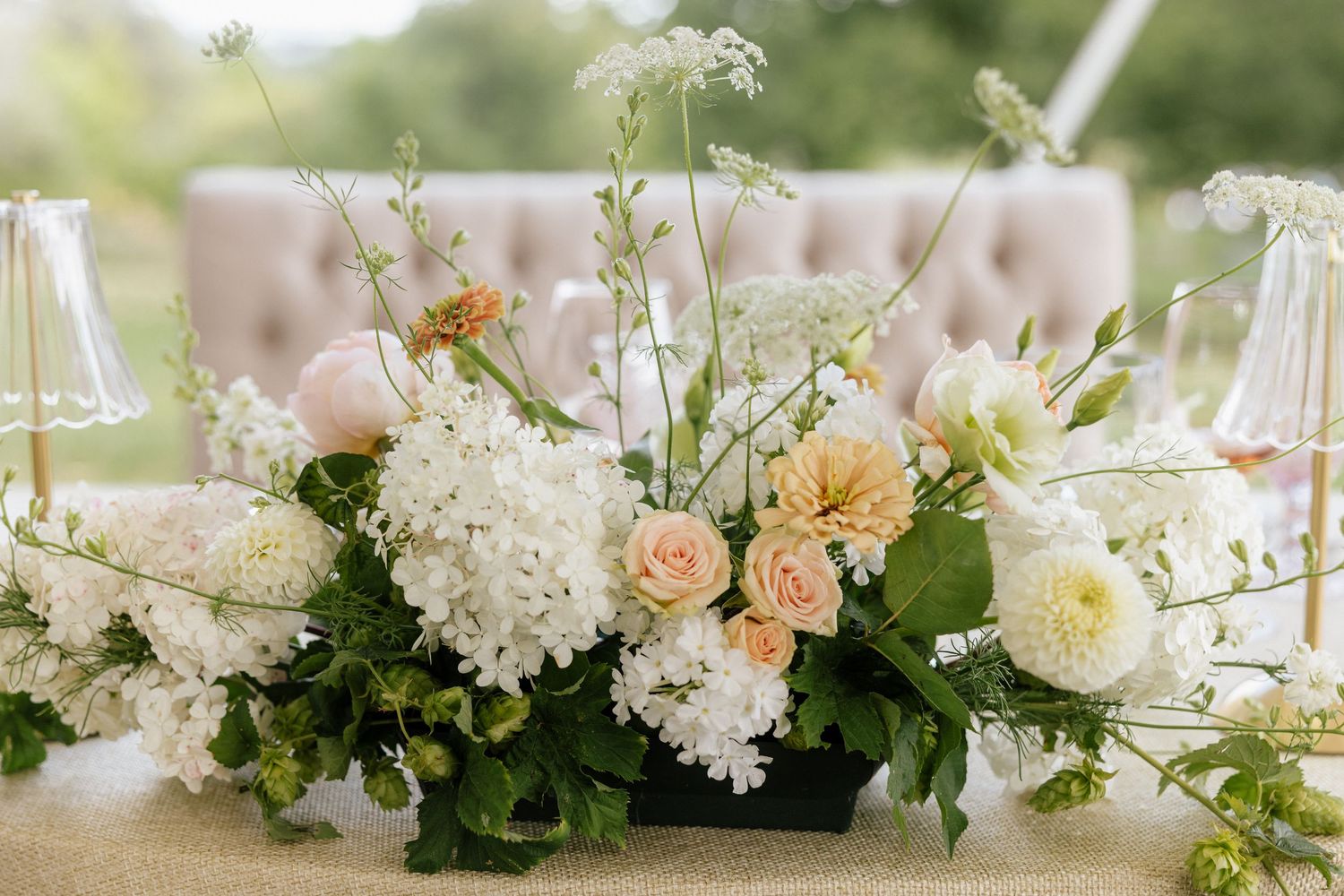 Elegant wedding centerpiece with white hydrangeas, peach roses, and greenery in a low arrangement on a reception table.