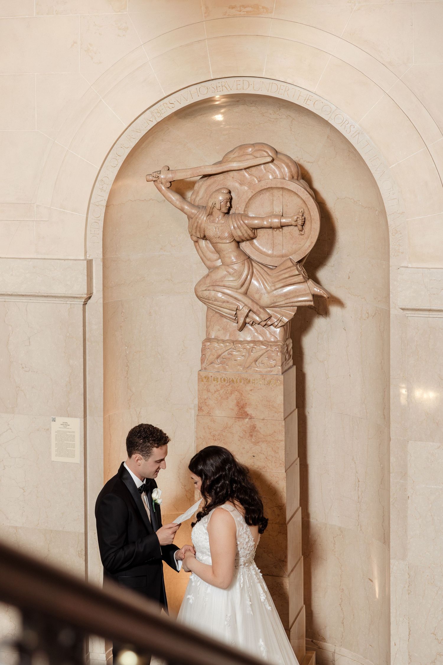 Bride and groom share private vows beside marble sculpture on staircase.
