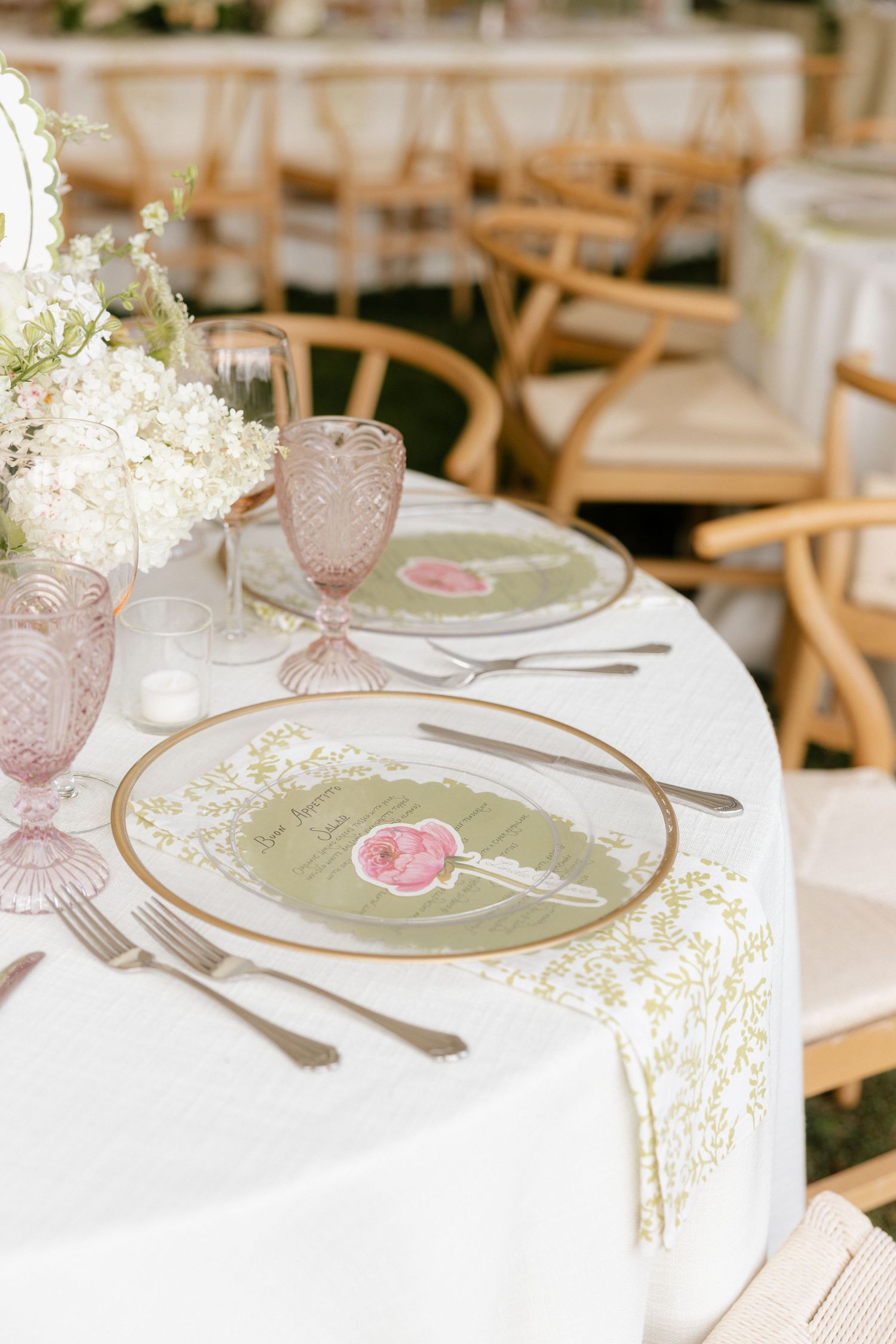 Elegant wedding table setting with sage green menus, pink roses, gold-rimmed plates, and pink glassware.