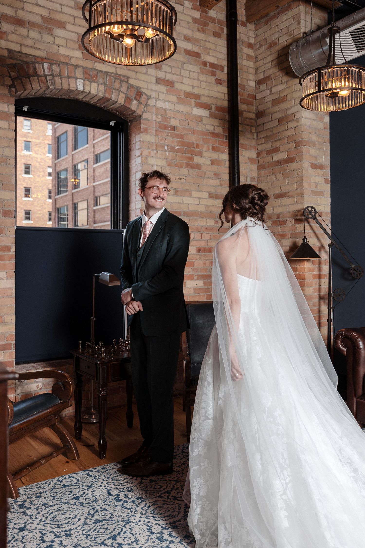 Groom laughs with delight as bride in lace gown and cathedral veil approaches during first look.