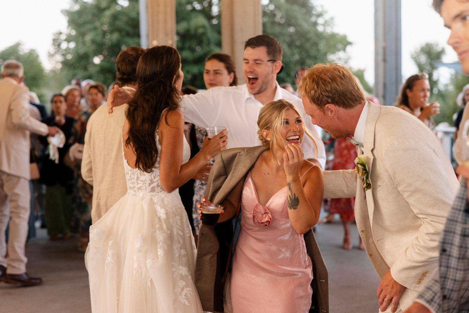 Joyful wedding guests laughing and celebrating with bride in white gown and bridesmaid in pink dress.