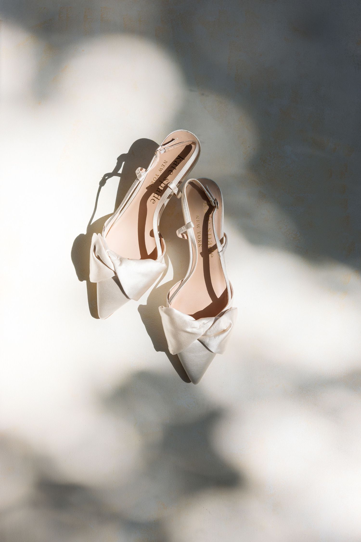 Elegant white slingback heels with pointed toes floating against a soft cloudy background in natural light.