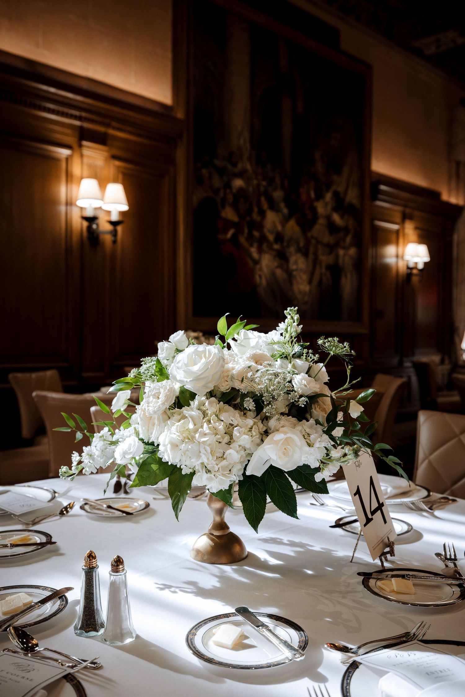 Elegant wedding table centerpiece with white roses and hydrangeas on a gold pedestal vase.