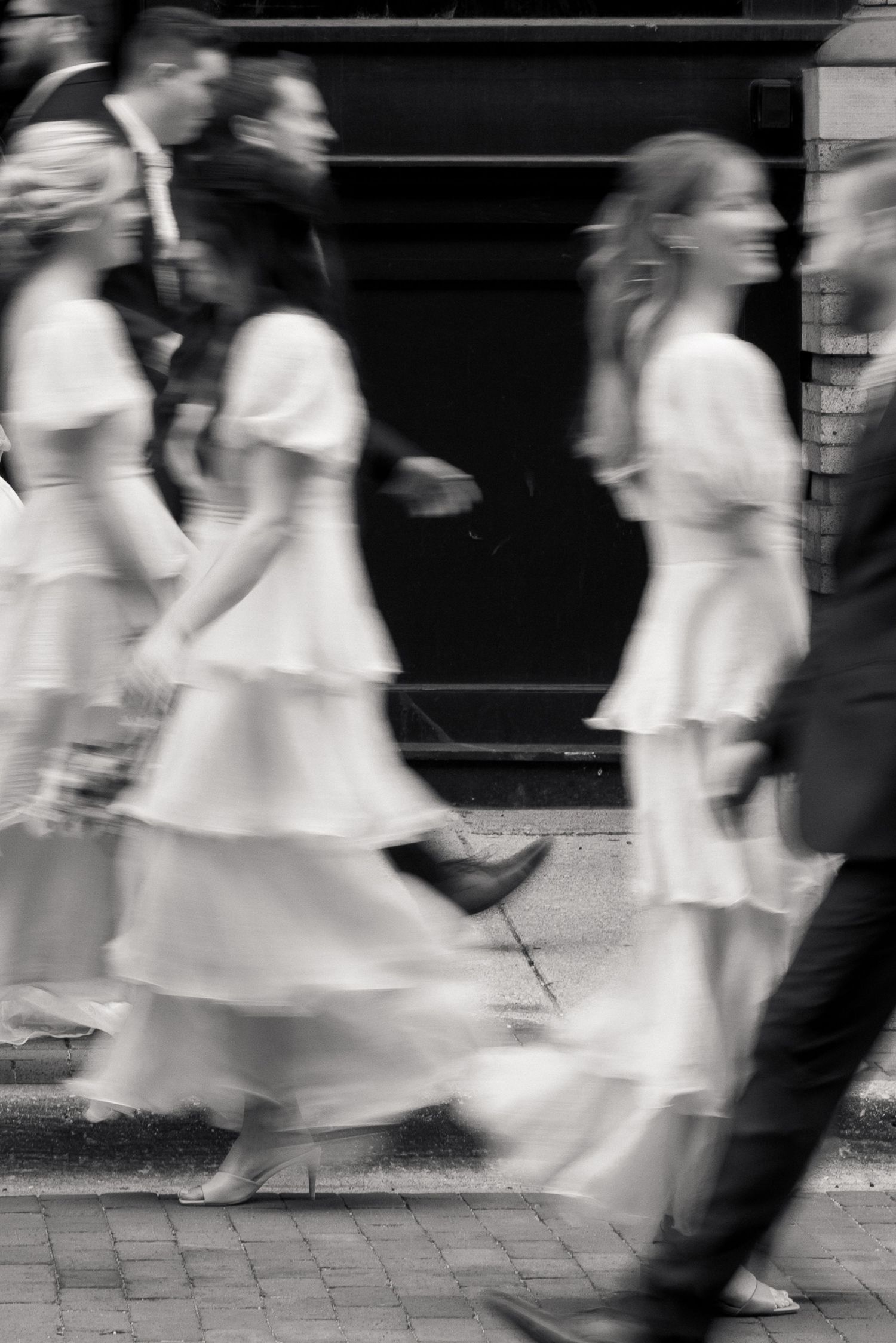 Black and white motion blur photo of bridesmaids in white tiered dresses walking outside wedding venue.