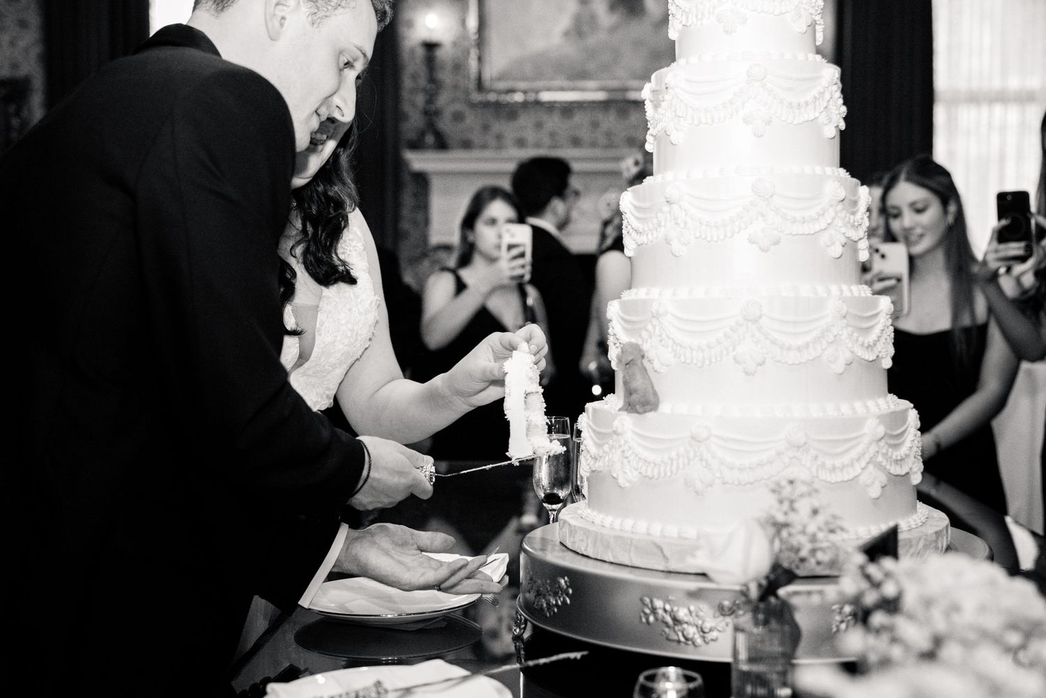 Bride and groom cutting their elegant white multi-tiered wedding cake in black and white photo.