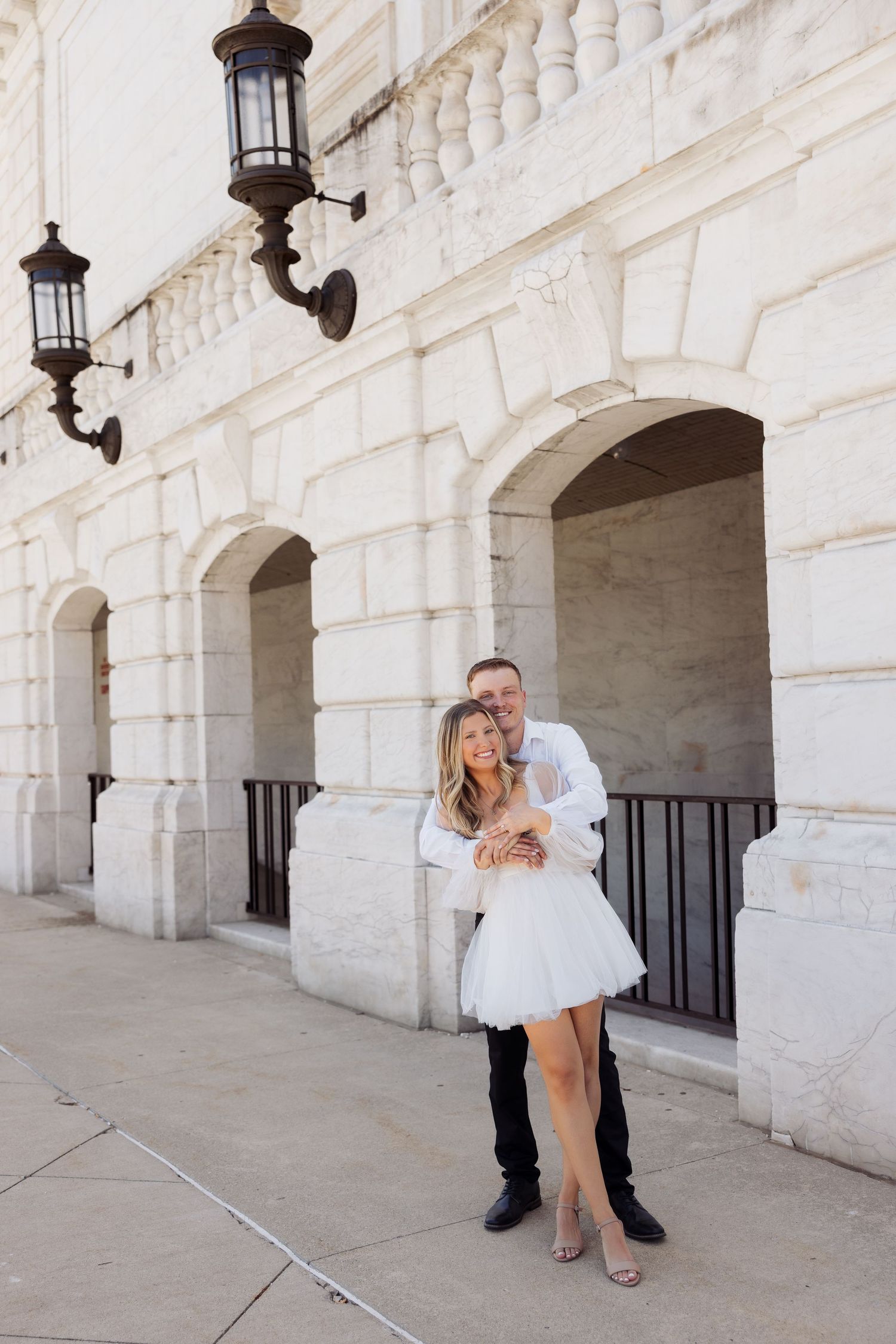 Couple posing in front of a white stone building with arched doorways and vintage lantern.