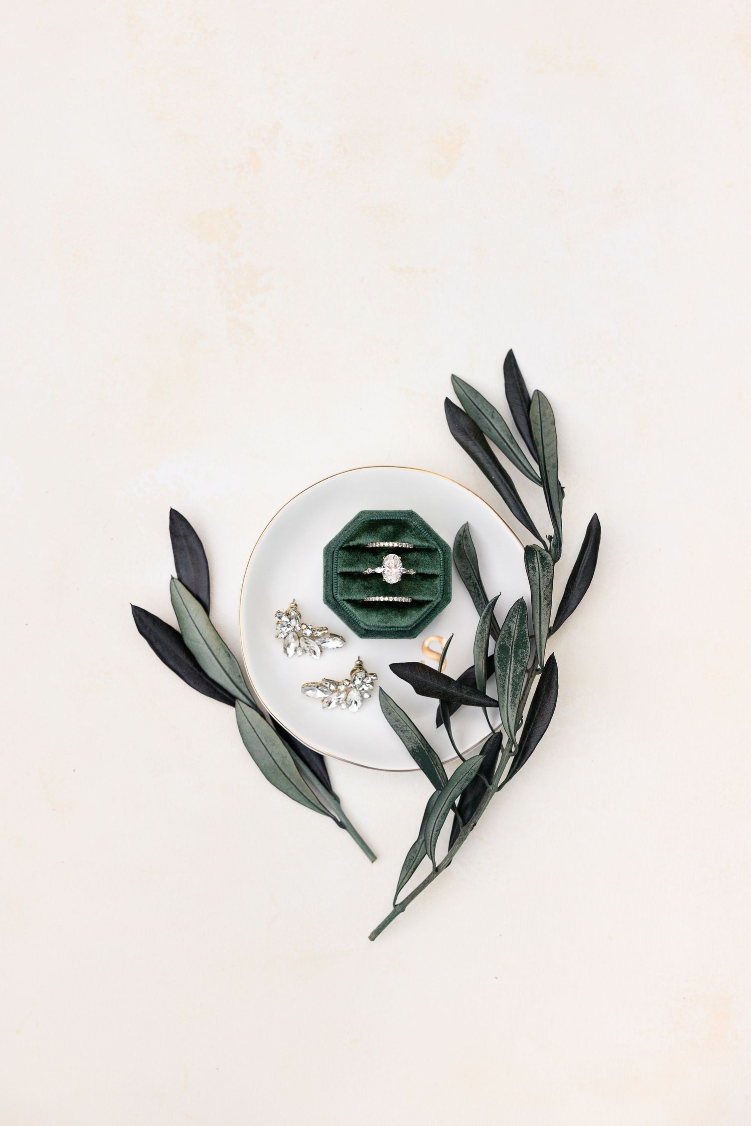 Diamond engagement ring in green velvet box displayed on white plate with earrings and olive branches.