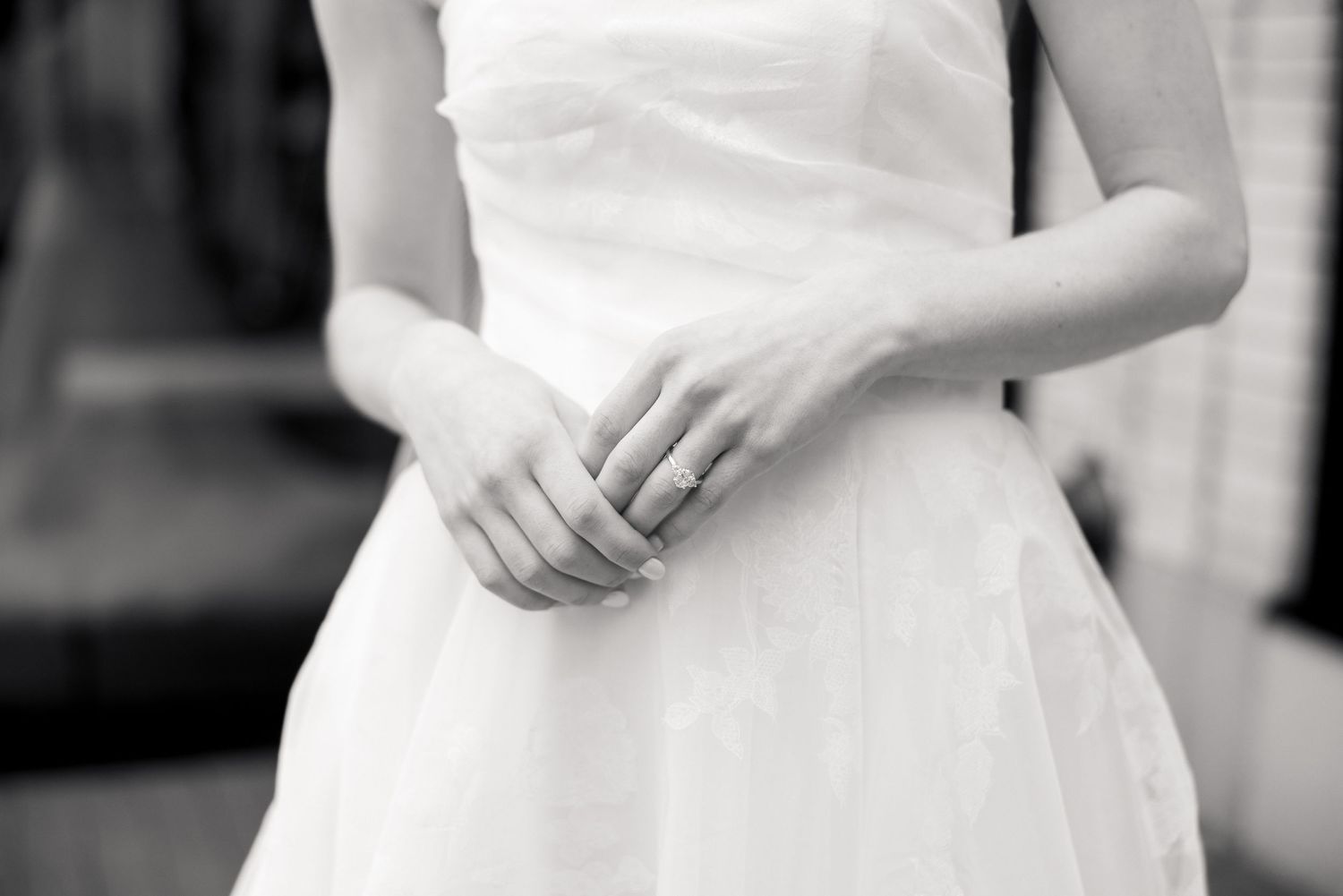 Black and white close-up of a bride's hands clasped together wearing a diamond engagement ring.