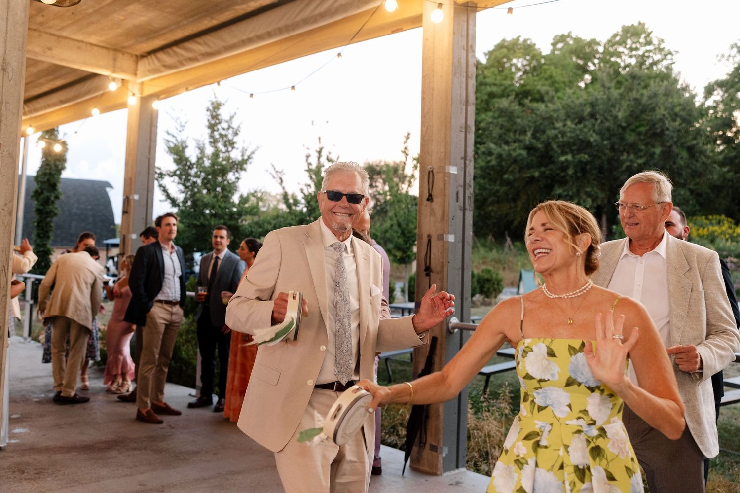 Guests smiling and socializing at an outdoor wedding reception venue with string lights and lush greenery.