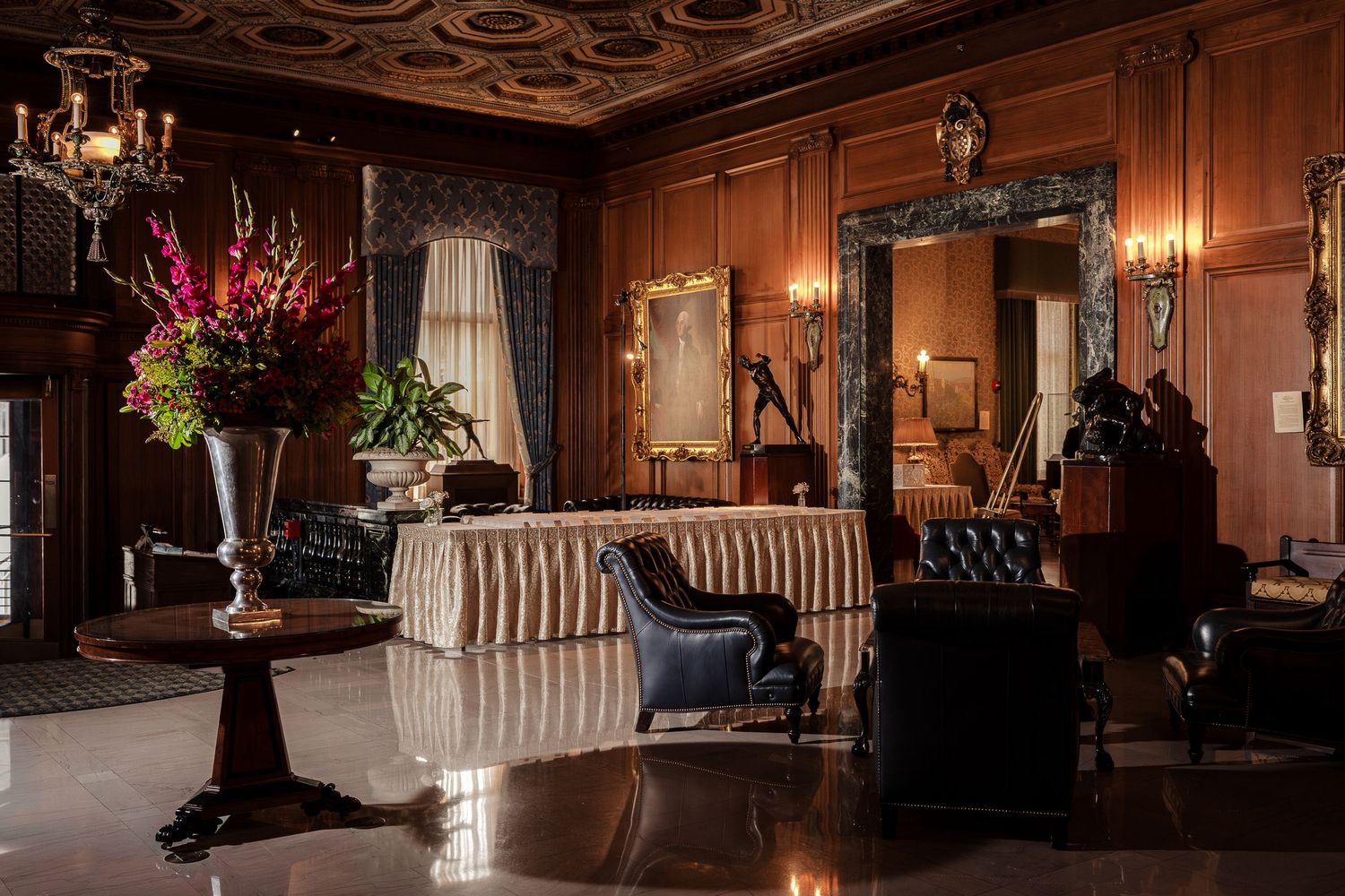 Elegant luxury hotel lobby with ornate wood paneling, tufted leather chairs, striped sofa, and grand chandelier in classic decor.