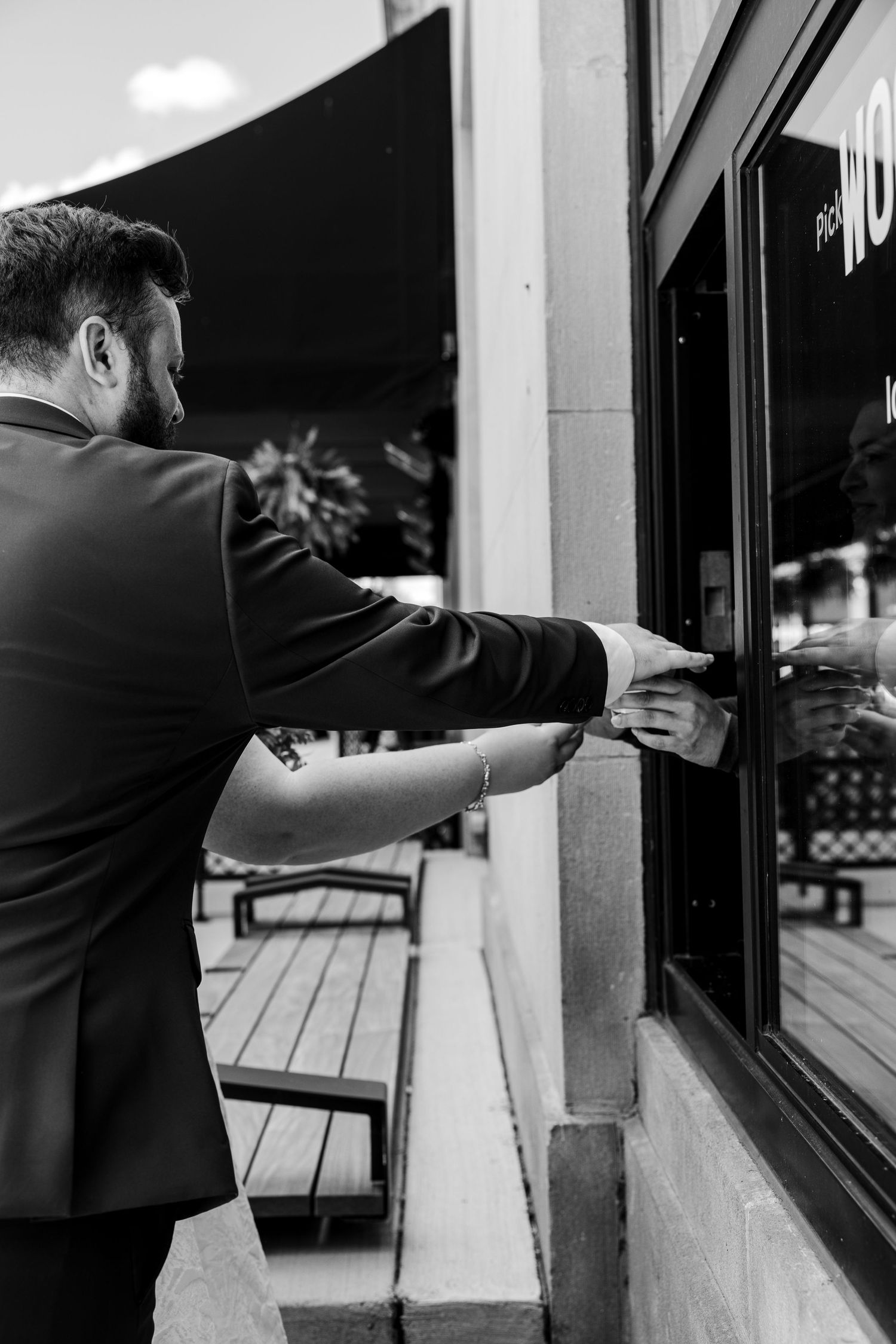 Man in suit reaching toward a restaurant window in a black and white outdoor photo.