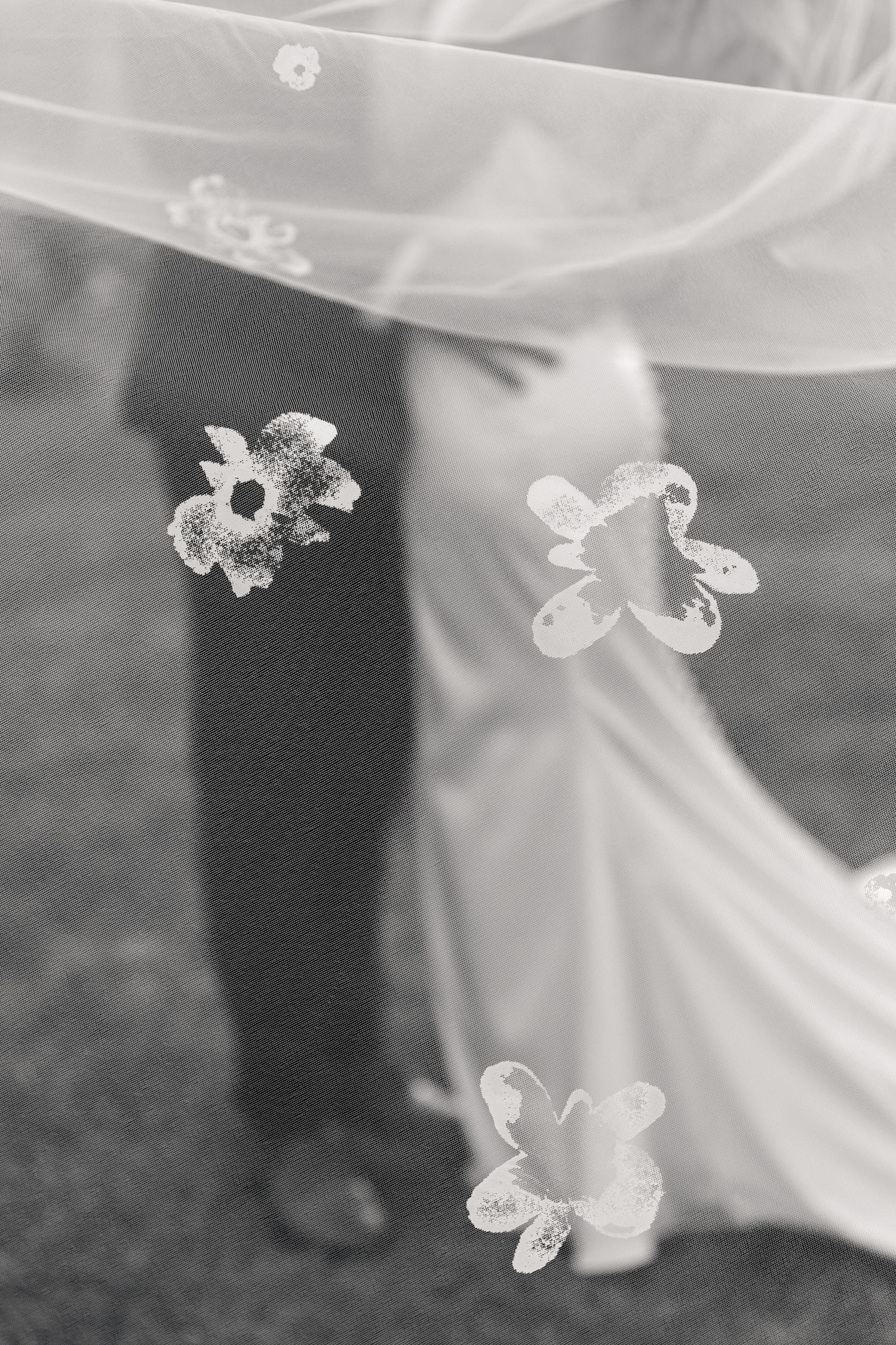 Black and white wedding photo of bride and groom through floral veil, romantic outdoor ceremony moment.