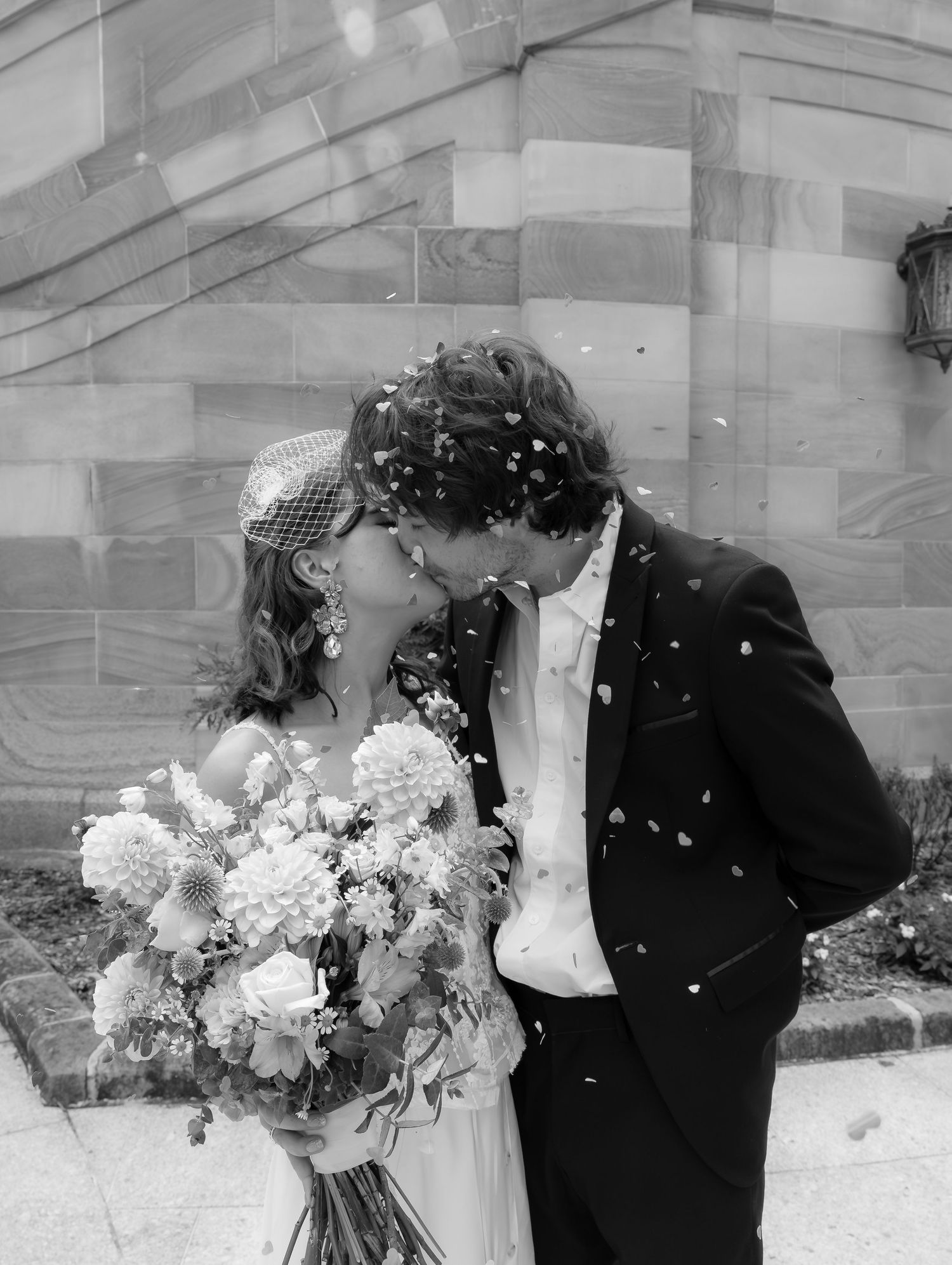 black and white image, couple kissing. Bridal holding bouquet of flowers and confetti in the air
