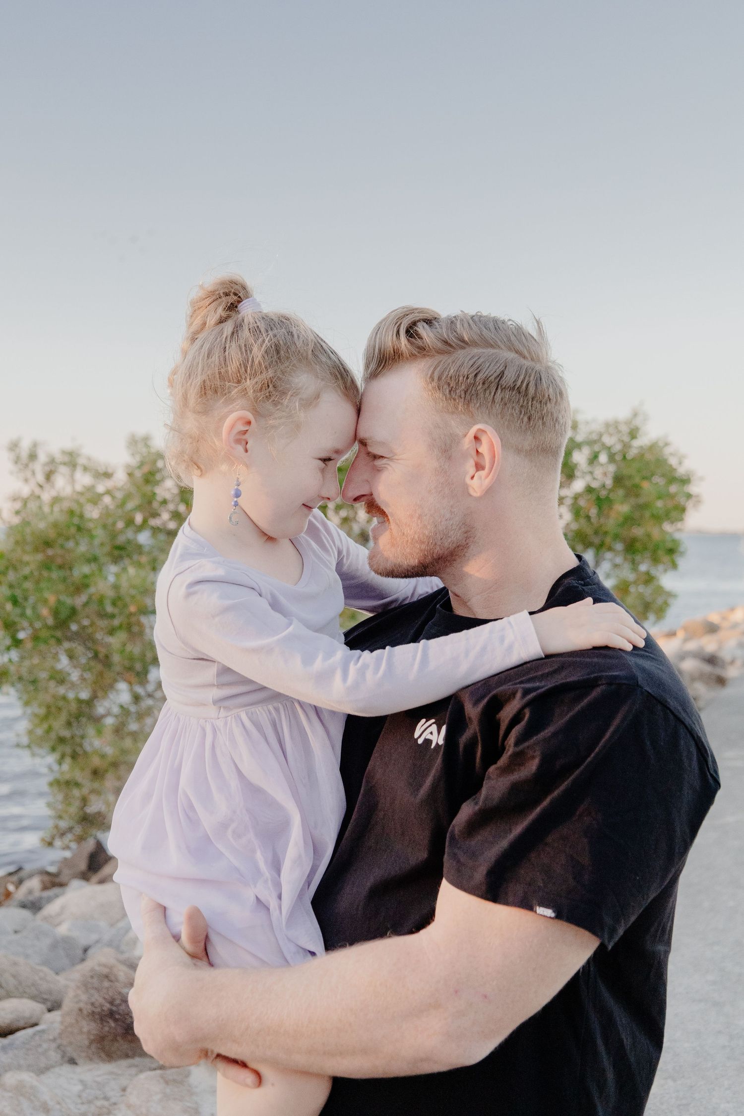dad and daughter image. dad holding daughter and they have faces pressed close while laughing