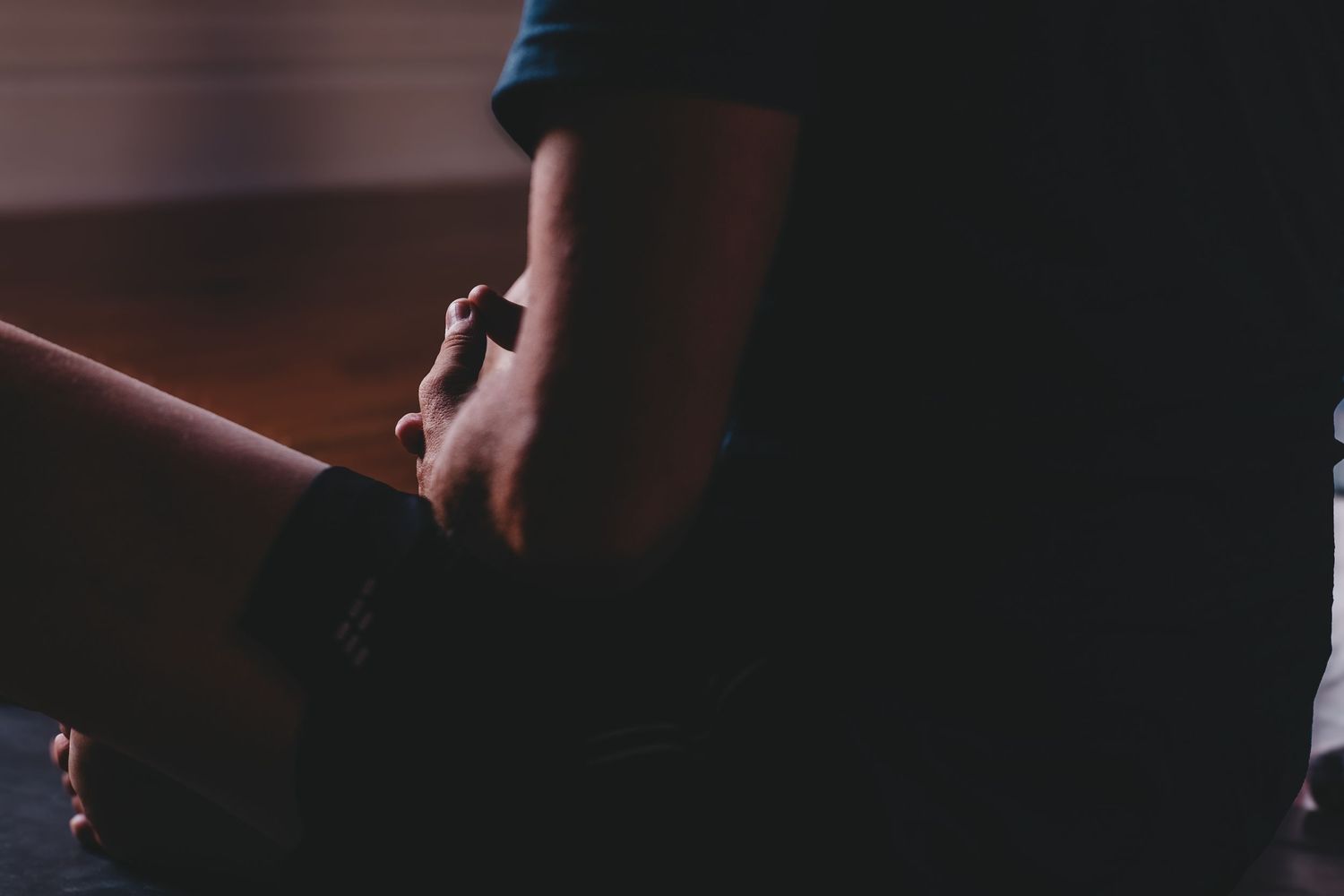 Close-up of two people holding hands in a dark, intimate setting with a watch visible.