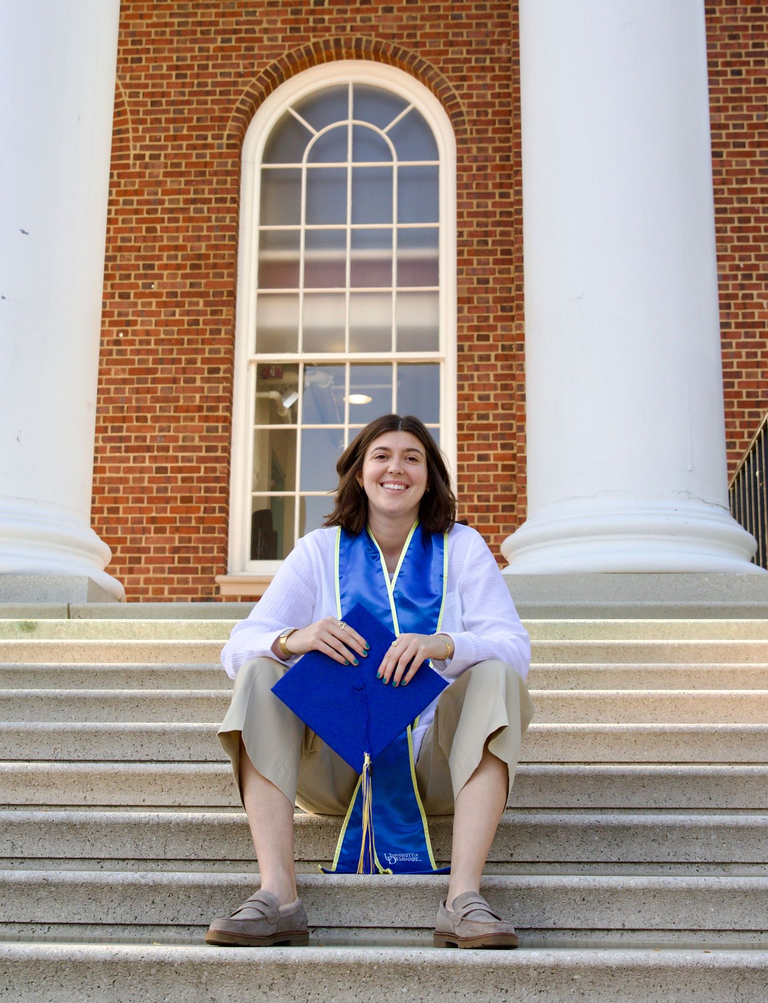 portrait of female university of Delaware graduate sitting on stairs of memorial hall