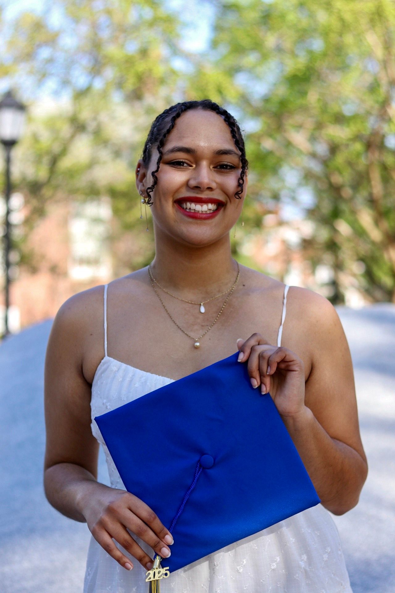portrait of female university of Delaware graduate in front of book statue, greenery in the background