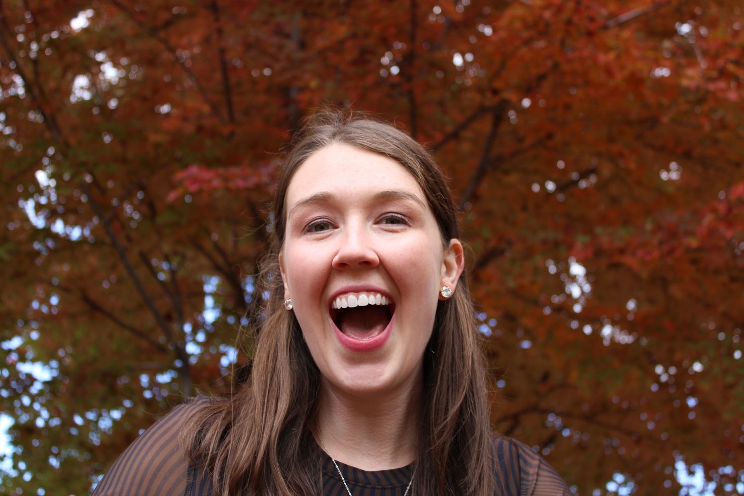 A joyful person laughs outdoors surrounded by vibrant autumn foliage and trees with red leaves | Sydney Allen Photography