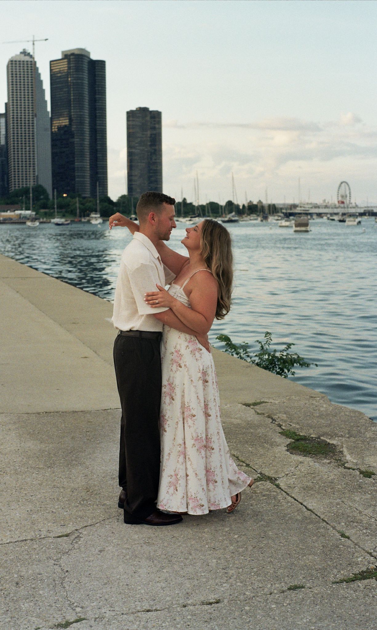 Couple embracing romantically on a waterfront promenade with Chicago skyline and Navy Pier Ferris wheel in the background.