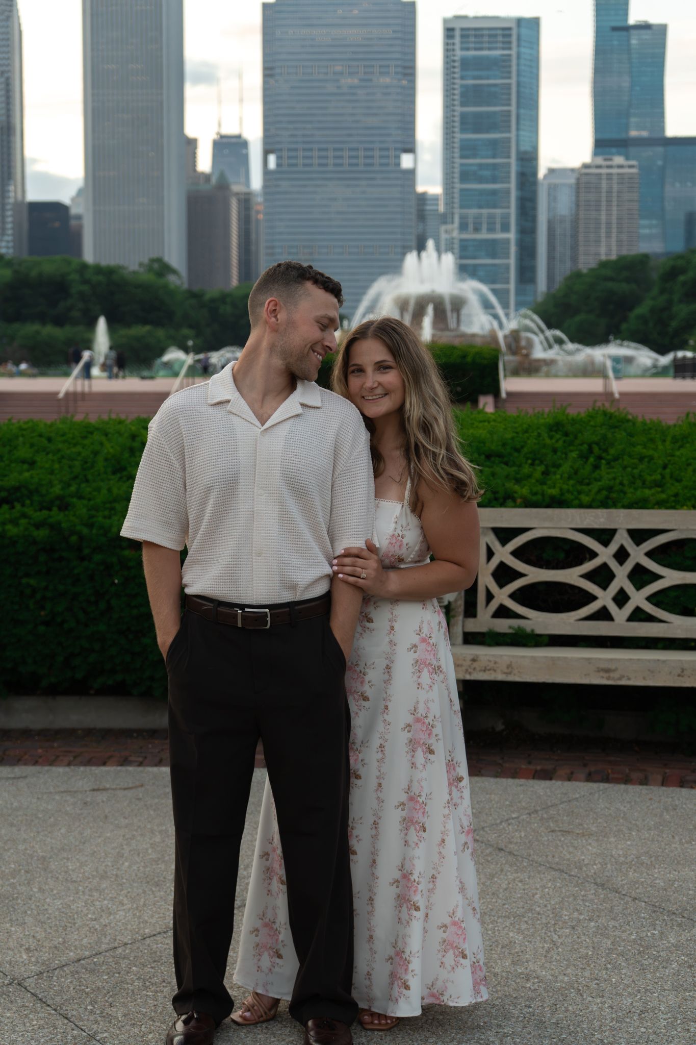 Couple posing in front of Buckingham Fountain with Chicago skyline backdrop, woman in floral dress, man in white shirt.