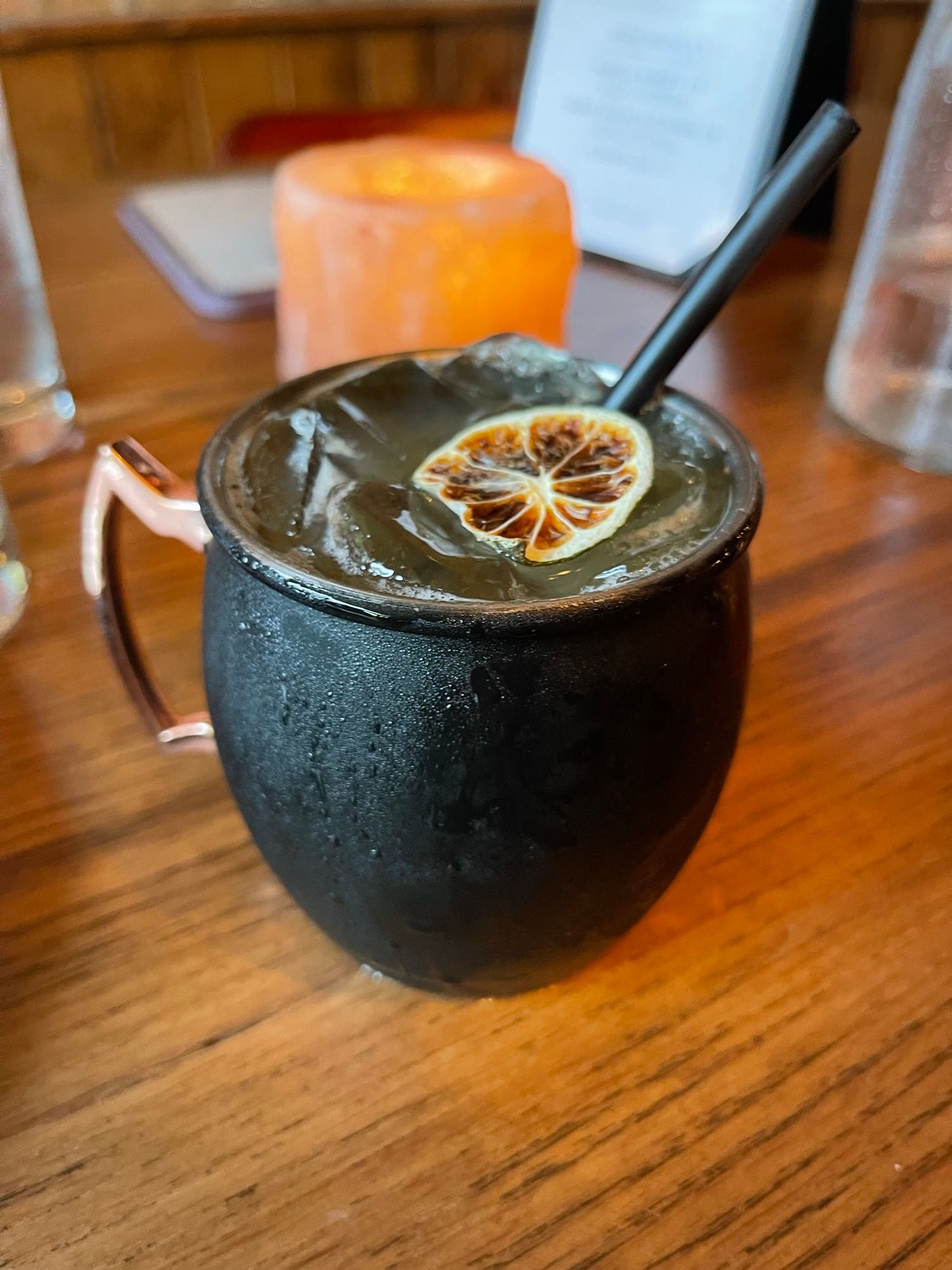 Dark Moscow Mule cocktail in black copper mug with dried citrus garnish and black straw on wooden table | Sydney Allen Photography