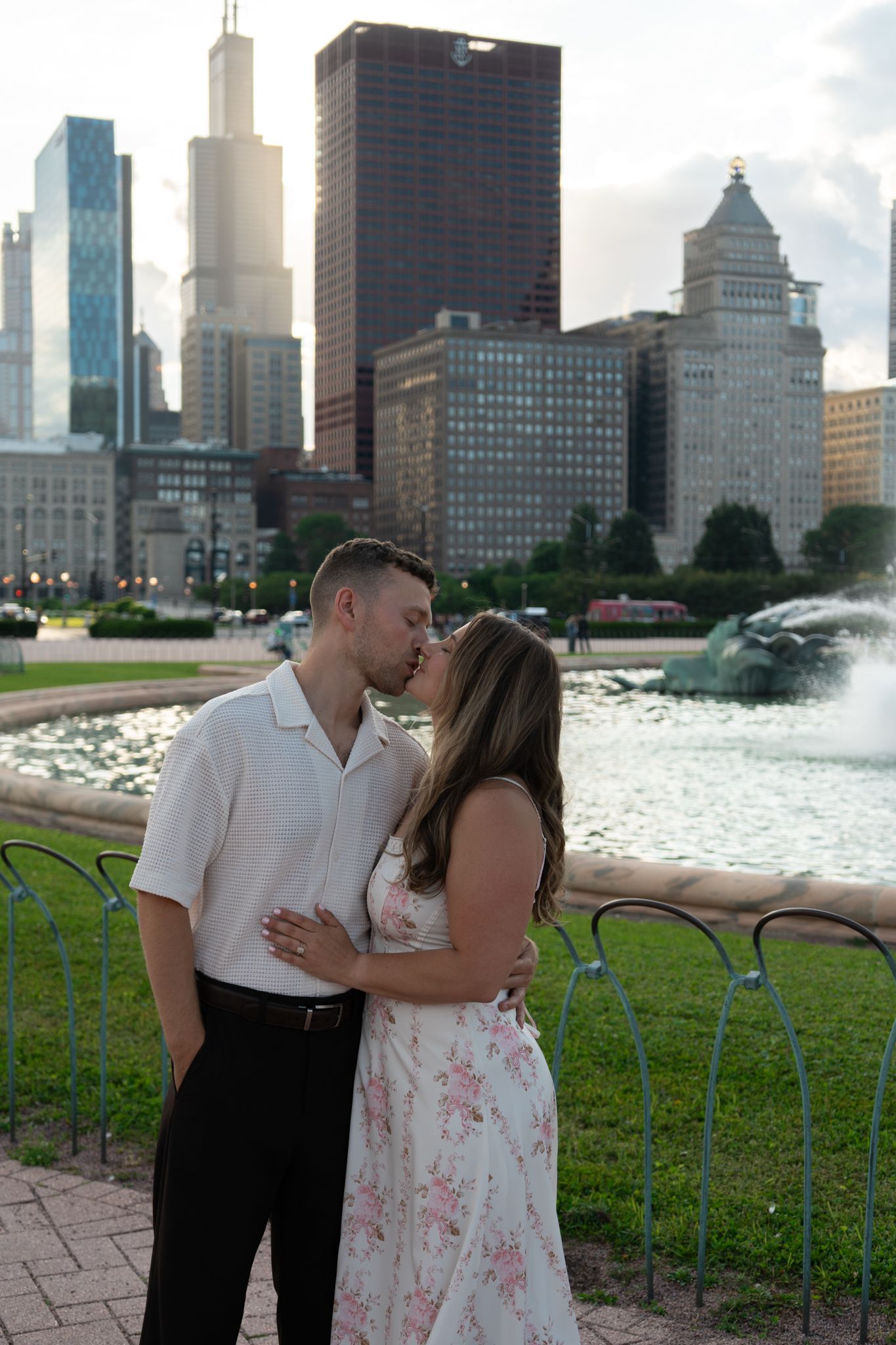 Couple kissing near Buckingham Fountain with Chicago skyline and Willis Tower in background.